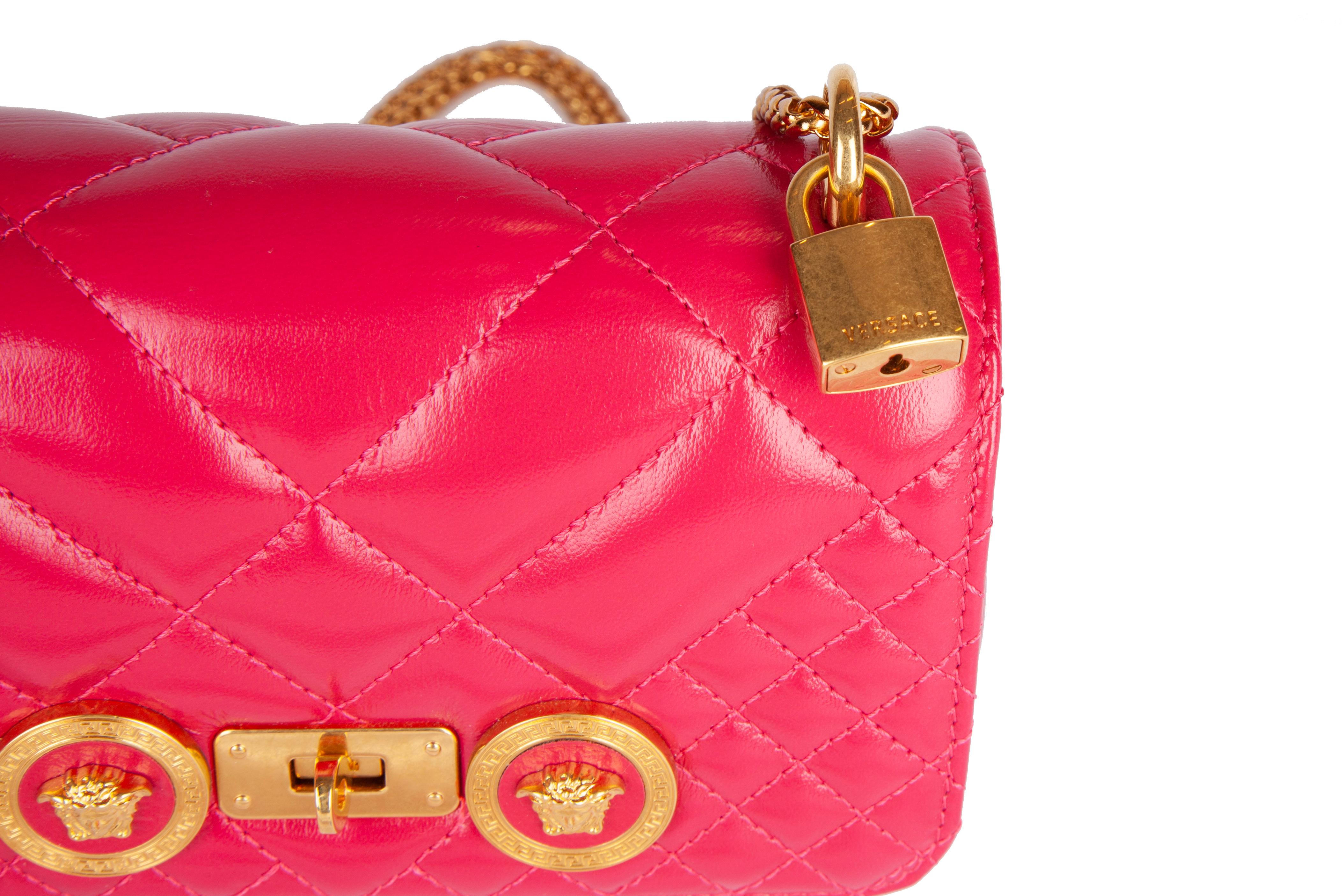 This Versace small fuchsia pink icon shoulder bag features quilted shiny calf leather, gold tone chain and hardware, a flap with medusa studs, a twist clasp, and one main compartment with a slip pocket. The small icon shoulder bag is both 