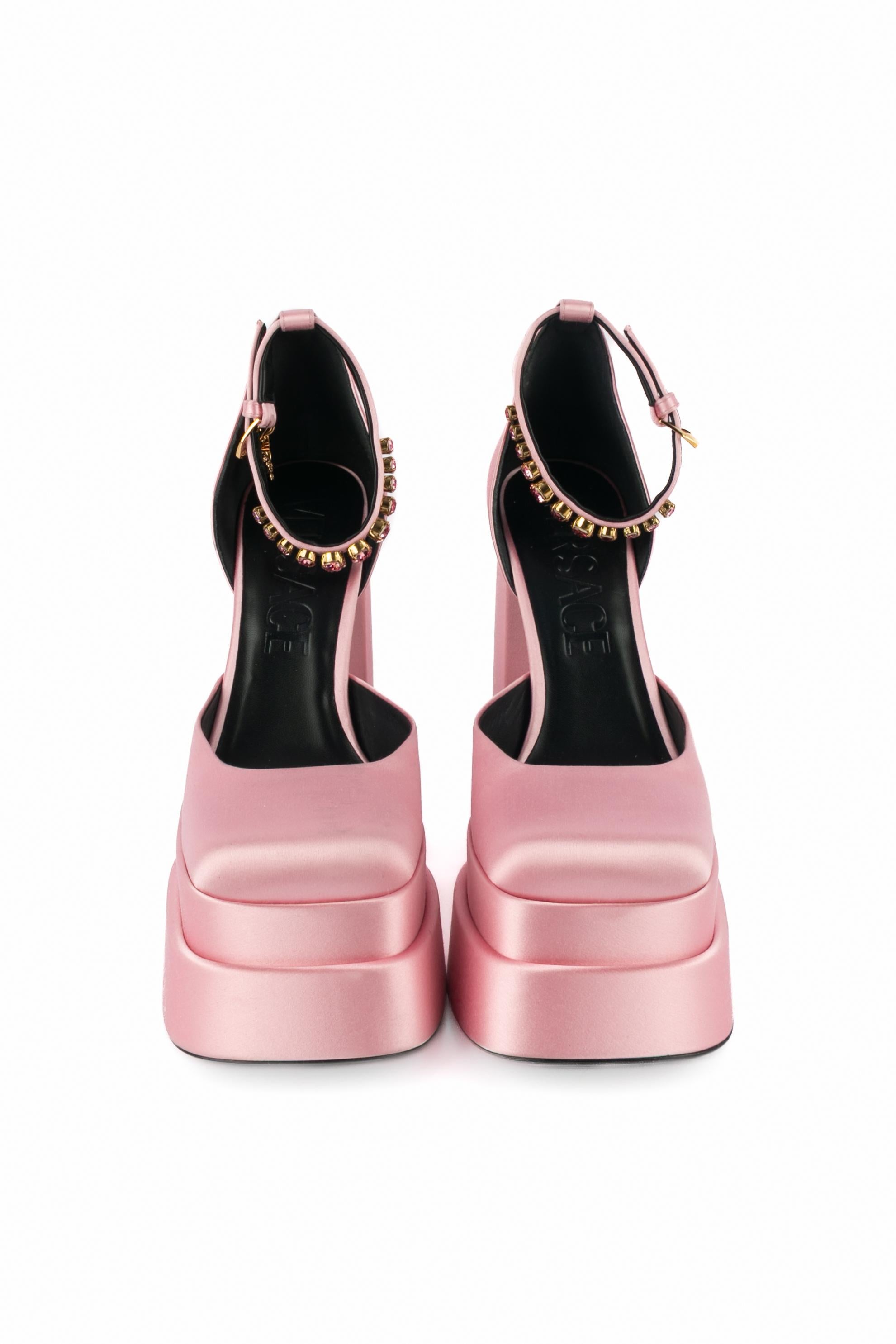 VERSACE - (Made in Italy) Hochhackige Stöckelschuhe aus blassrosa Satin mit zweistufiger Plateausohle. Die Handgelenkszaumzeugs sind mit rosa Strasssteinen verziert und mit goldenen Metallcharms in Form von Medusen verziert. Größe 40FR angegeben.