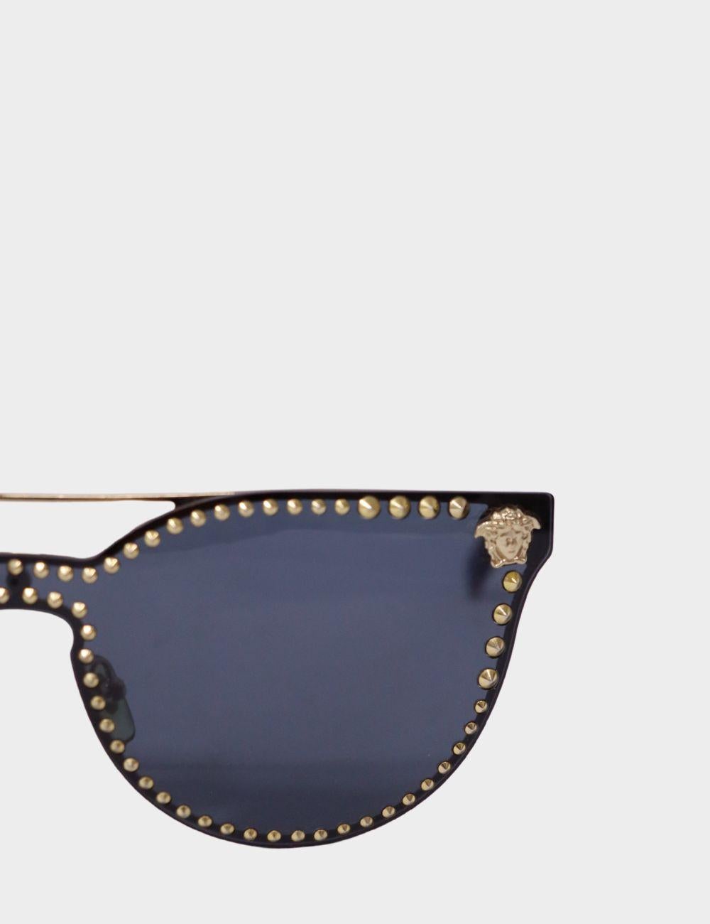 Atrae todas las miradas con el auténtico lujo italiano de estas gafas de sol de ojo de gato con tachuelas Versace. Con una atrevida montura negra, los icónicos herrajes de Medusa en cada patilla y unas brillantes tachuelas doradas que recubren las