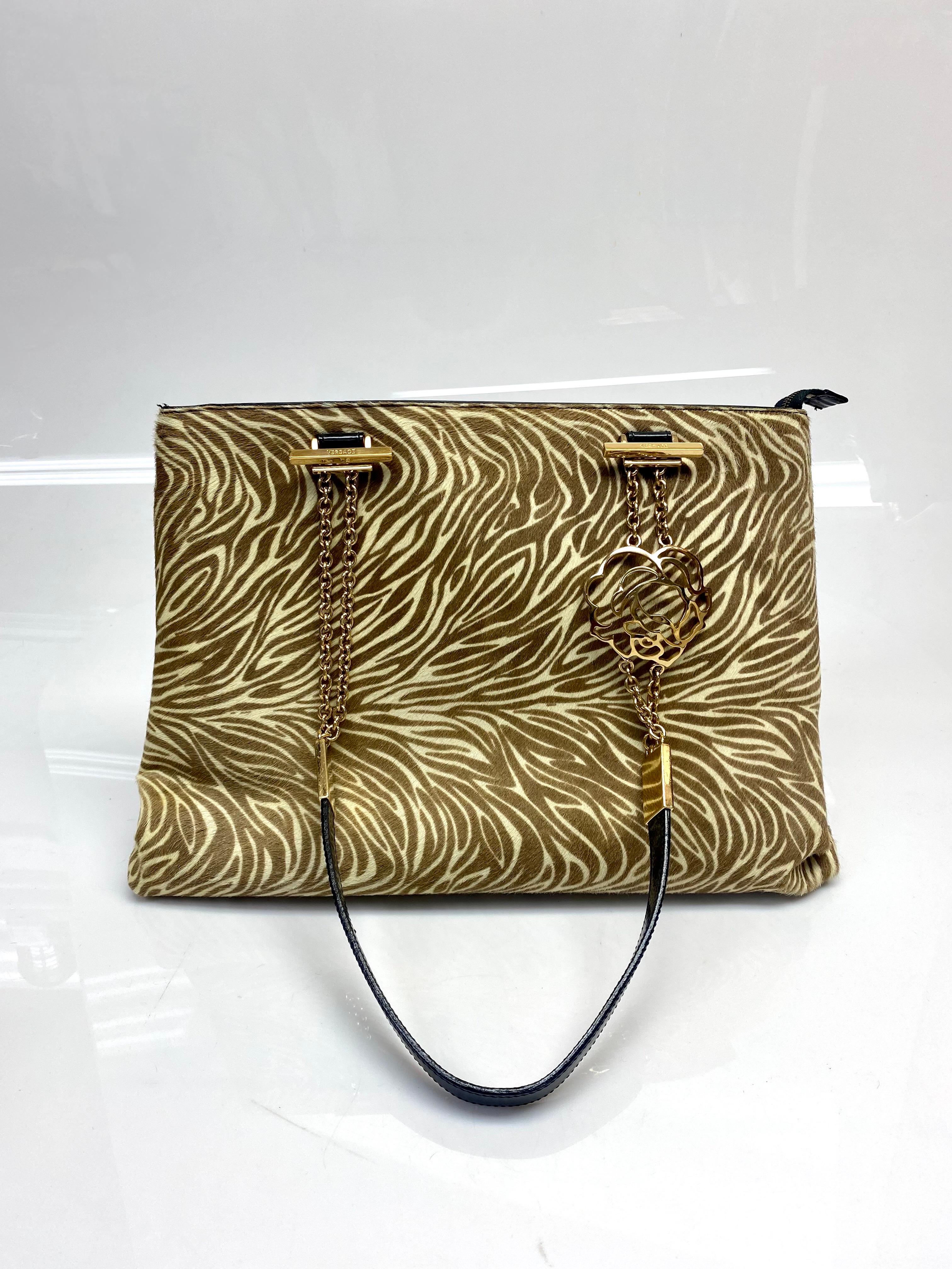 Versace Vintage Animal Print Pony Hair Shoulder Bag. This Versace shoulder bag is animal printed pony hair. Inside, there is a zippered pocket. The straps are black patent leather with gold colored chain and rose shaped detailing. This bag is in
