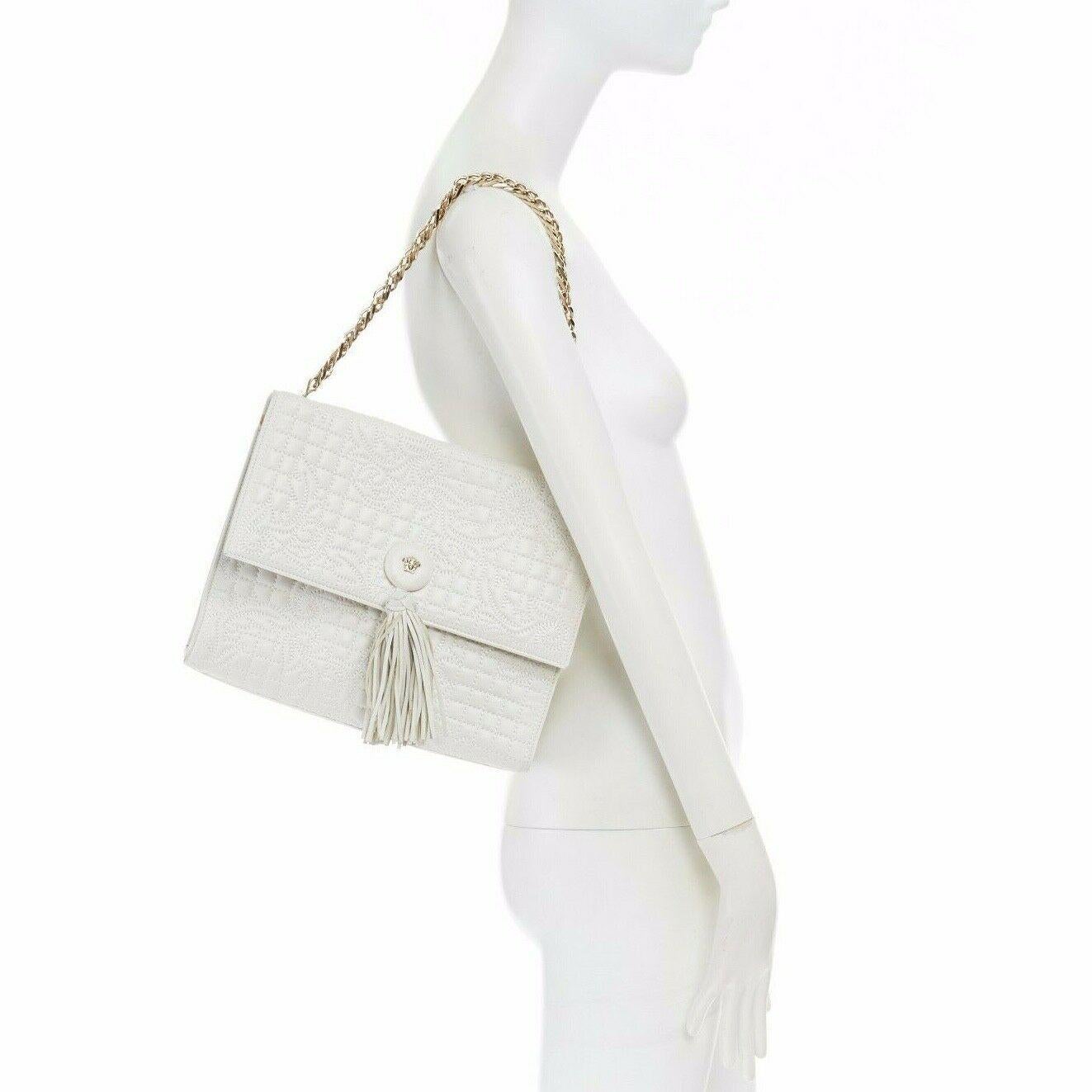 GIANNI VERSACE
Vanitas collection. White nappa leather. Baroque quilted design on leather upper. Medusa head with fringe tassel design at front flap closure. Magnetic closure. Gold-tone metal chain linked shoulder strap. Single wall zip compartment