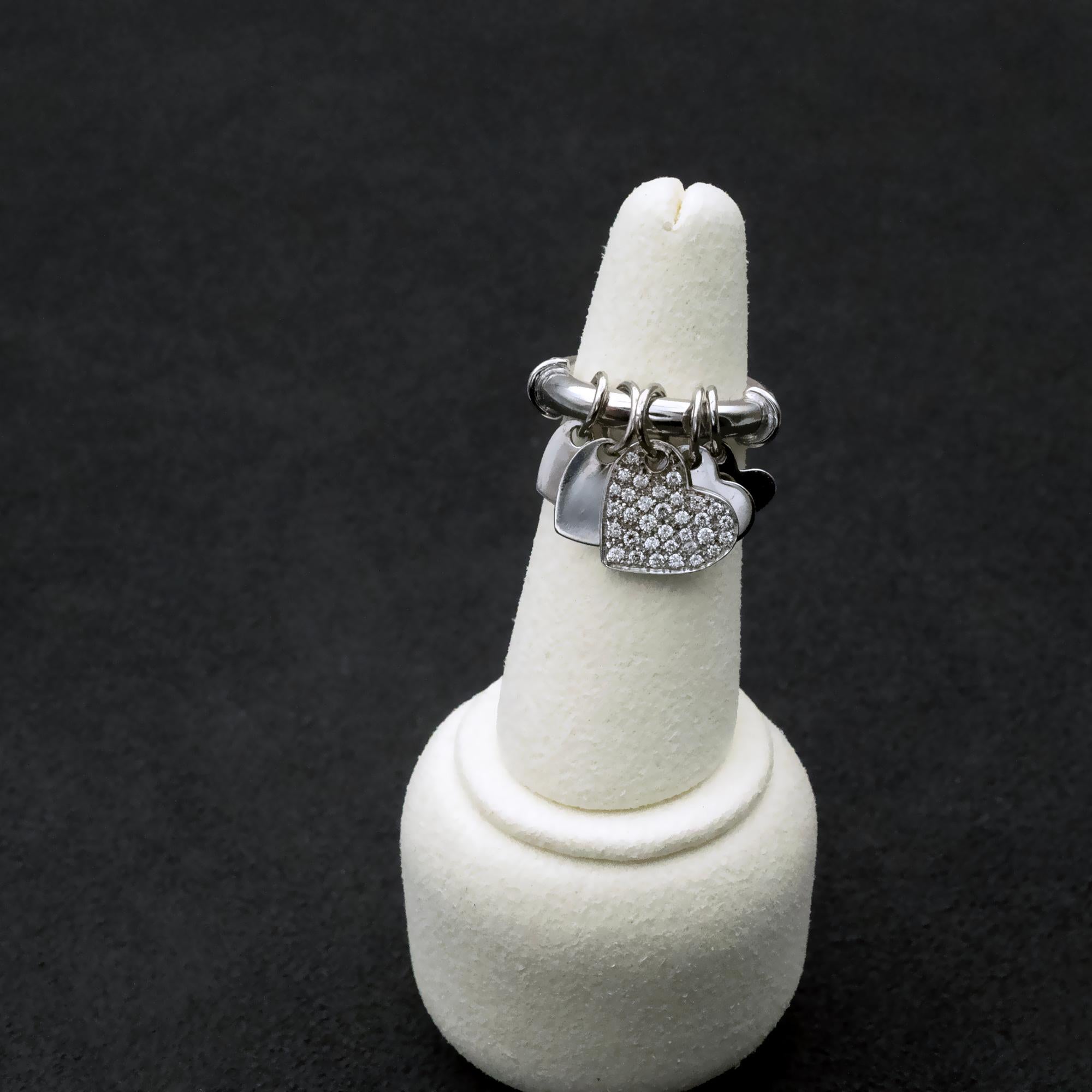 This lovely modern 18K white gold charm ring is a true statement of elegance and versatility. Designed with a contemporary yet timeless aesthetic, it features a collection of heart-shaped charms, including a dazzling pavé-set diamond heart that