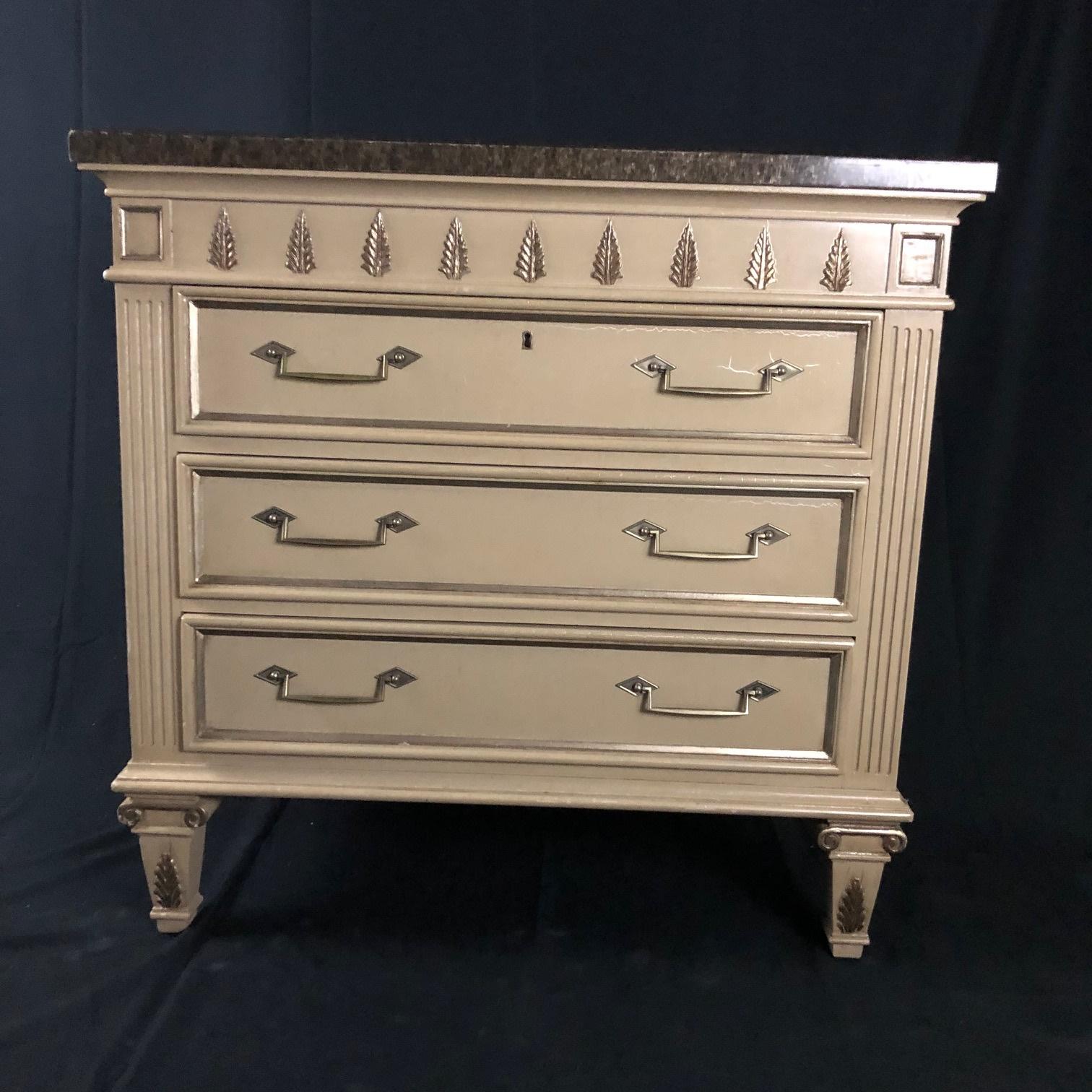 A large and handsome pair of painted mid century chests or night stands constructed of heavy solid wood, painted in an off white mottled finish with faux marble and glass tops having broad silver gilt accented aprons over long drawers. Versatile and