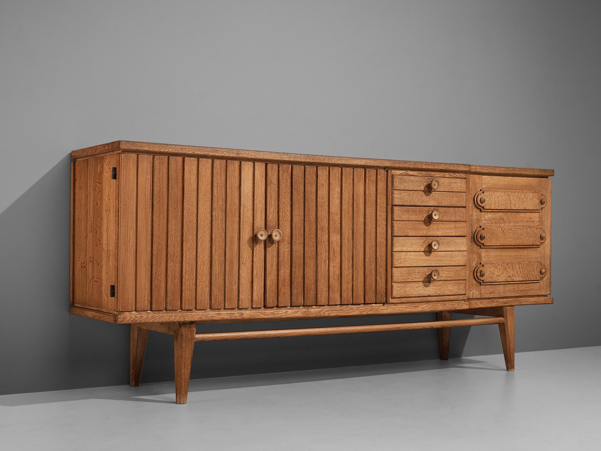 French sideboard, oak, France, 1960s

With the vividly designed fronts and the functional and versatile storage facilities this high-quality sideboard serves both visual and practical aspects. A section of drawers is flanked by one door with