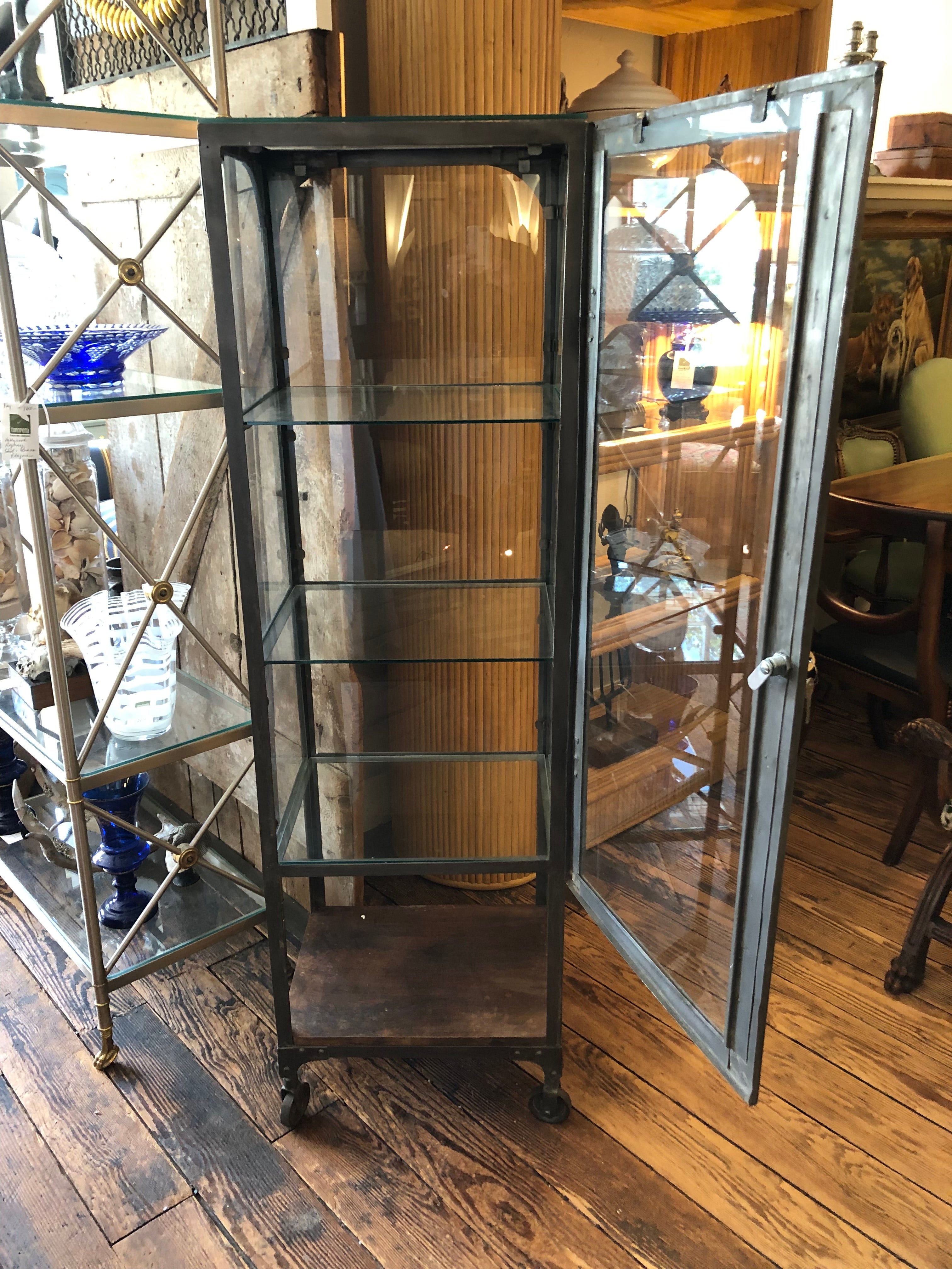 Multi functional cool looking vintage grey steel medicine cabinet having glass door, sides, top and shelves.  Lower tier is wood and the whole vitrine rolls easily on wheels.  Great in a bathroom for towels and toilet paper, etc.  Or an artist's