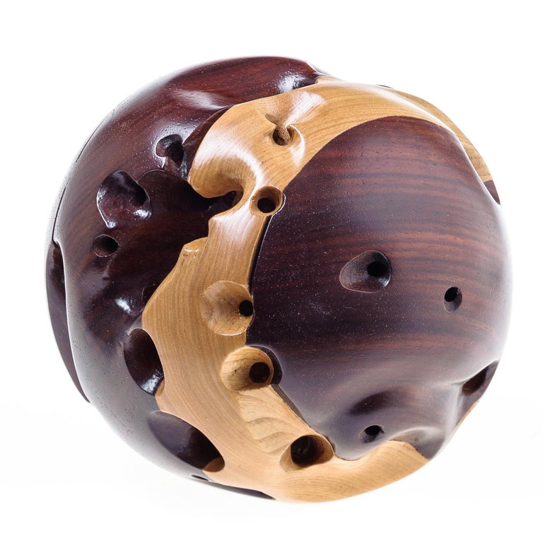 A true masterpiece, this exceptional sculpture embodies the timeless elegance and versatility of wood. The spherical sculpture is composed of layers of ash with its delicate straw color and paduka with its deep red hue, entirely hand carved and