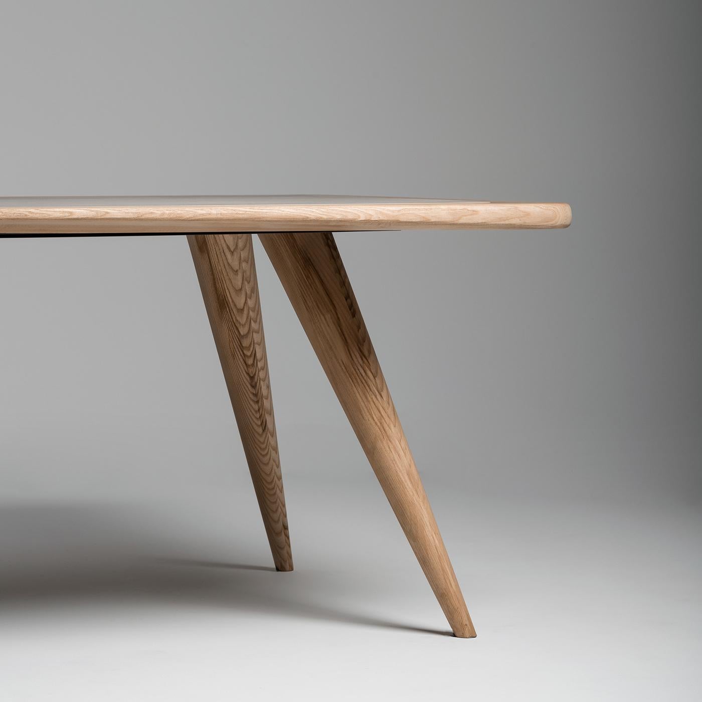 The search for sinuosity and movement is the origin of the supple, almost elastic profile of the table. The supports of the top open and project outwards with their conical, simple, and decisive shape. The natural finish of the wood and the use of