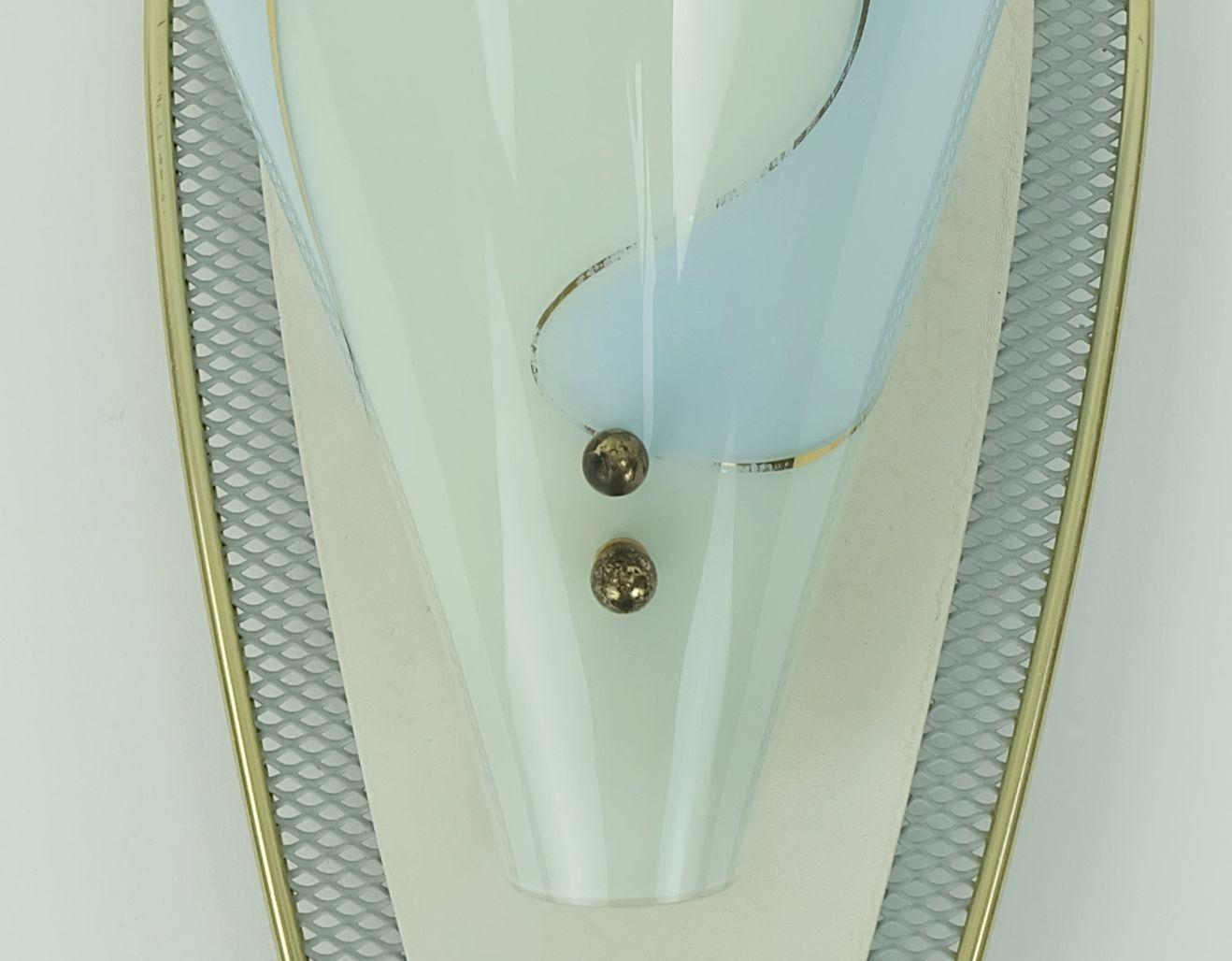 A very beautiful mid century sconce. Made of white lacquered metal wire with brass rim. Center piece matte beige lacquered metal. Glass shade in light blue and green with gold colored lines. For one E14 bulb (no bulbs included in the