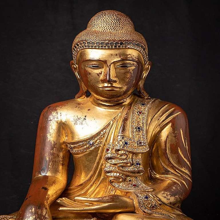 Material: wood
63,5 cm high 
52,8 cm wide and 38 cm deep
Weight: 18.9 kgs
Gilded with 24 krt. gold
Mandalay style
Bhumisparsha mudra
Originating from Burma
19th century
With inlayed eyes
With Burmese inscriptions on the base.
 