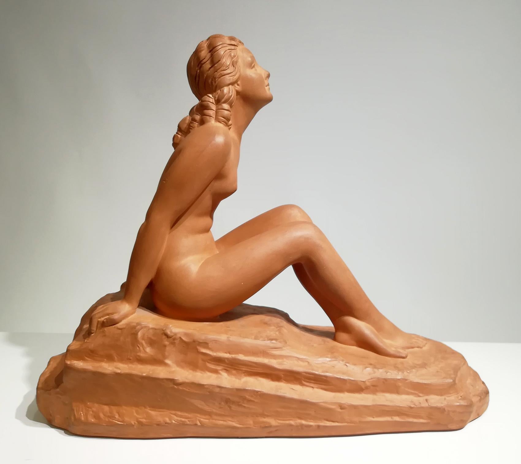 D. H. Chiparus Art Deco Terracotta sculpture entitled 'Dreaming' of a naked woman sitting on an inclined lot with her knees partially bent towards her.
She is leaning forward a little and her hands rest on the floor behind elegantly sculpted by