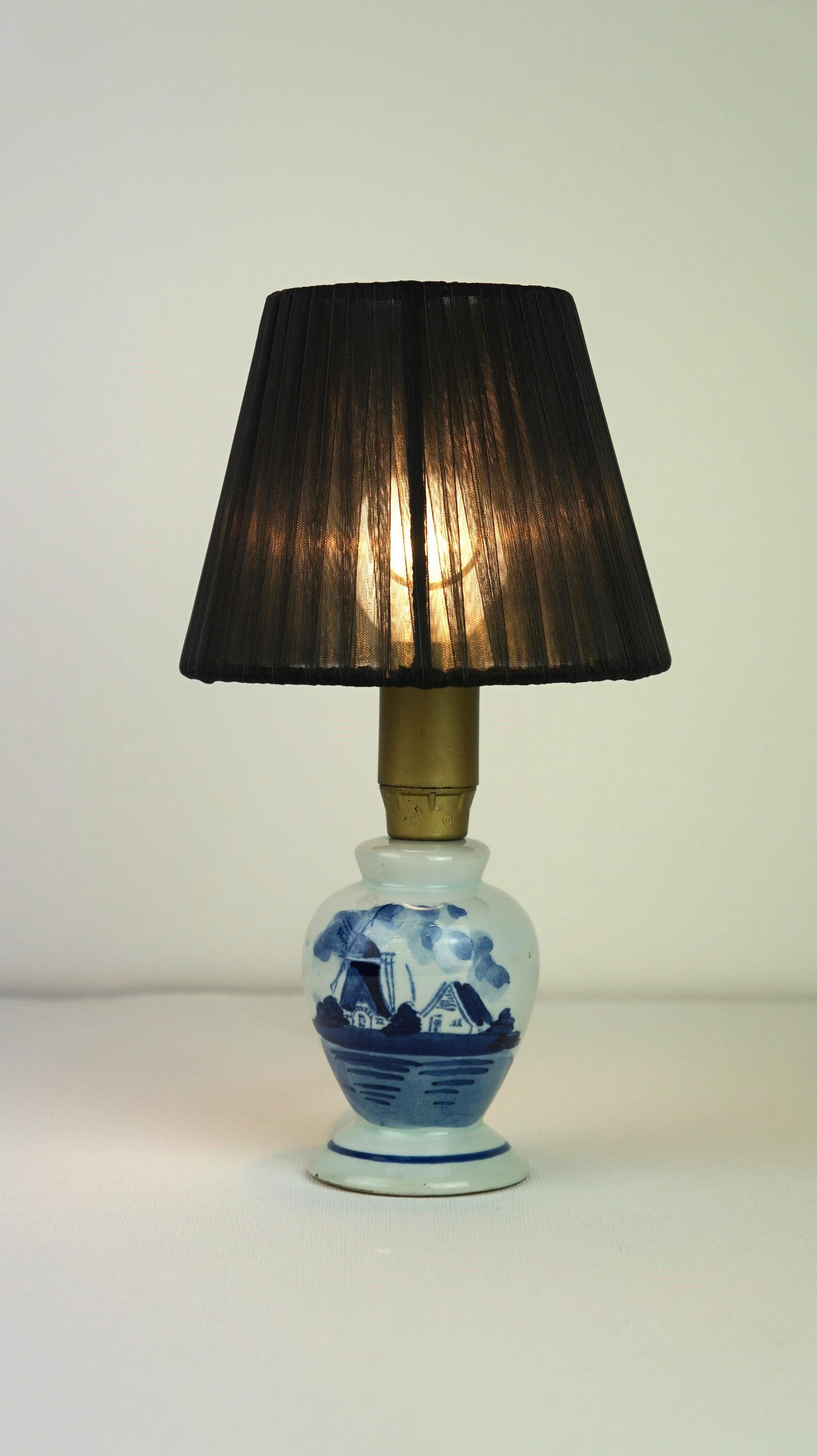 Offered: this very charming Delft blue ceramic lamp with a windmill design.

A true eye-catcher for enthusiasts. This delightful Delft blue lamp features a quintessentially Dutch image and a lovely classic pleated shade. It is in good condition and