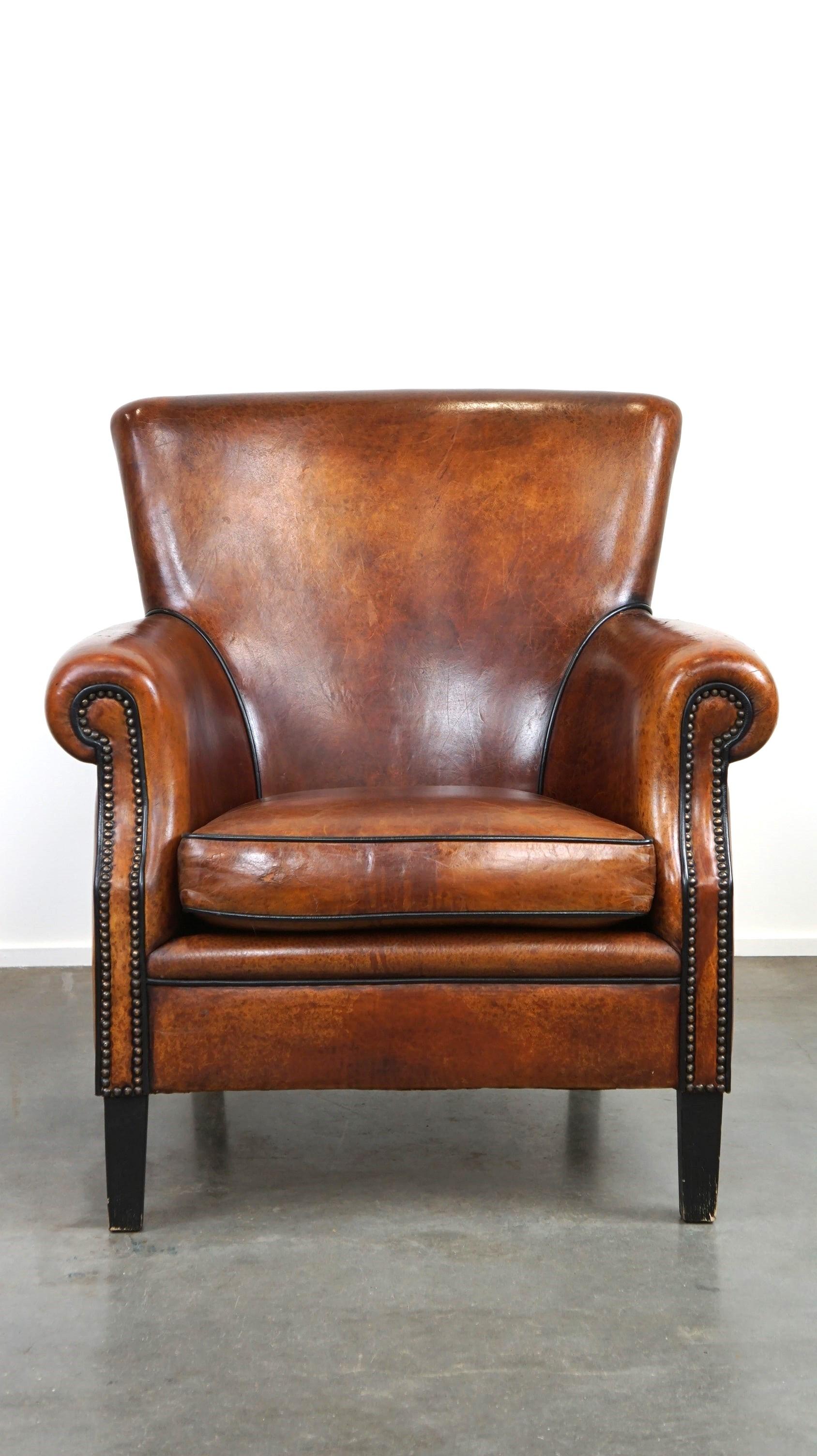 Offered: this very comfortable classic sheepskin leather armchair with beautiful warm colors, adorned with decorative nails and contrasting piping.

This armchair is an easy favorite, with few people finding it anything but comfortable. Despite some
