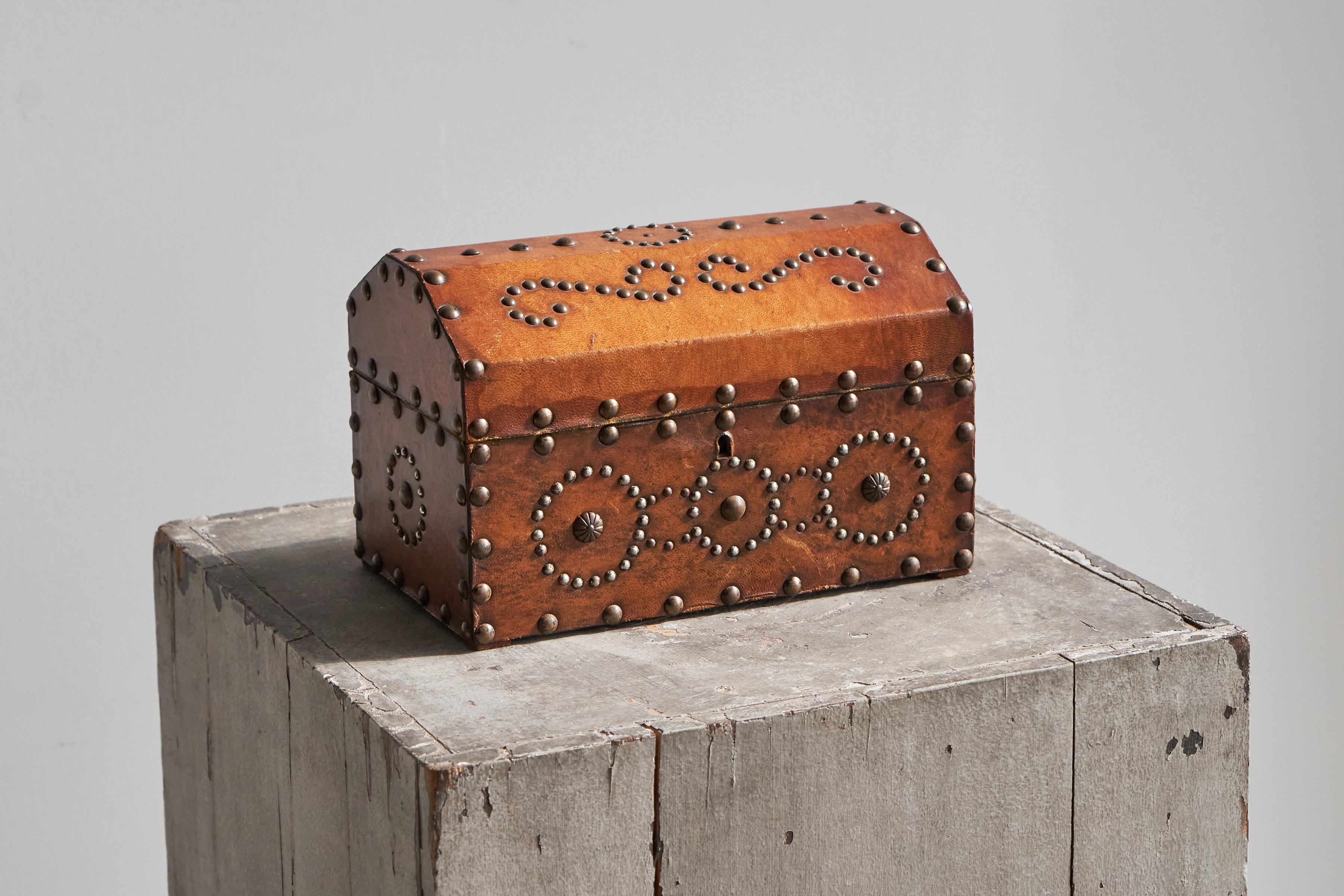 Sehr dekorative Box aus Leder und Metallnieten, Europa, 1950er Jahre.

Diese dekorative Box aus der Mitte des Jahrhunderts ist mit warmem, braunem Leder überzogen und weist komplizierte Nietenverzierungen auf. Die Schachtel hat einen gewölbten