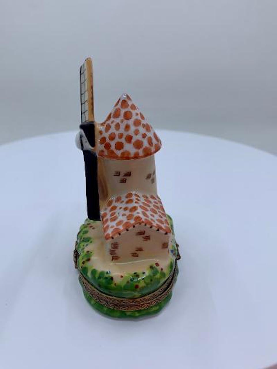 Collectible and very unique, Limoges porcelain miniature trinket box is handmade and hand painted in France and features a whimsical and very detailed Dutch grain windmill surrounded by a garden like setting with a vining tree growing up the side of