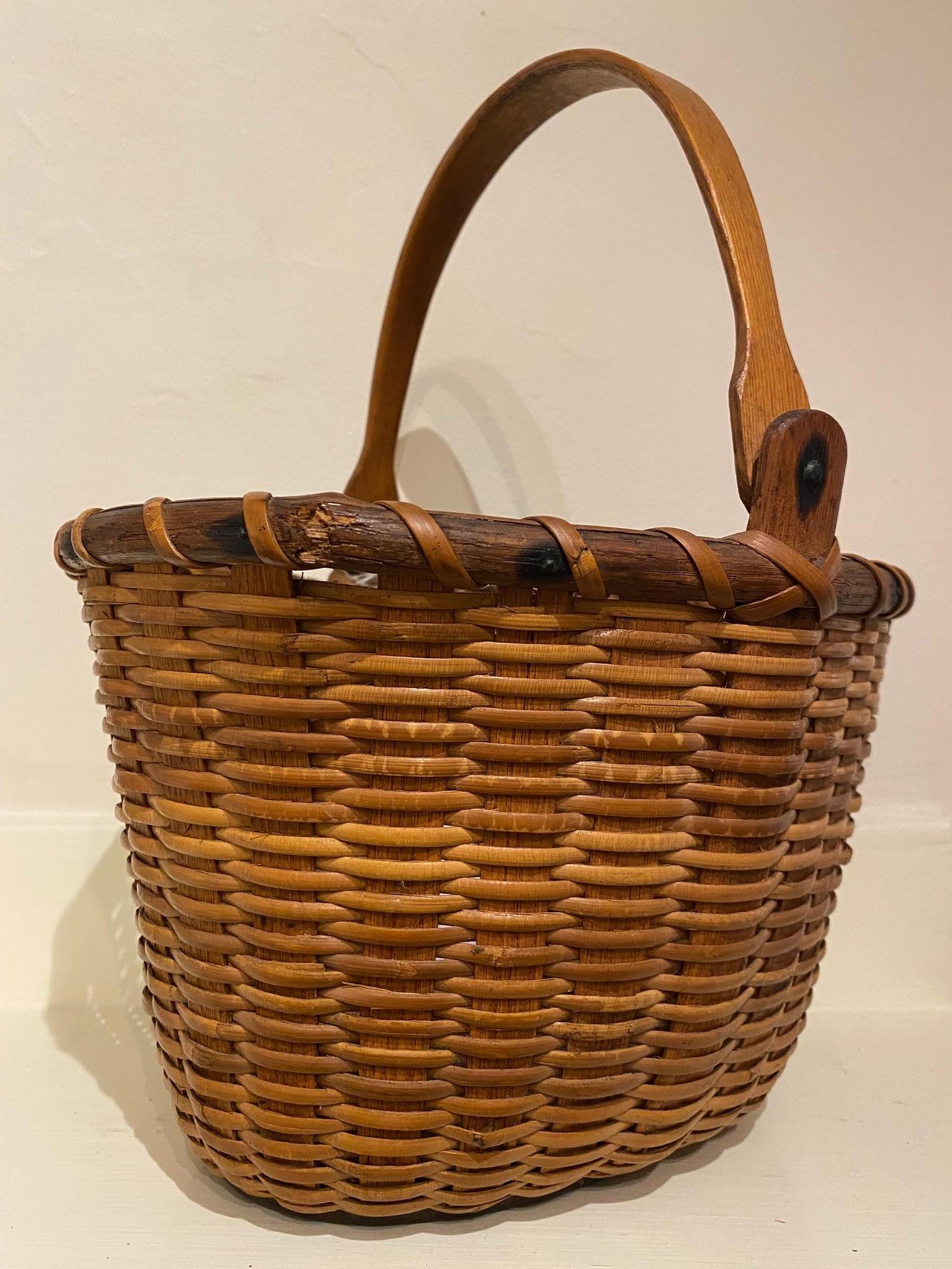 Very Early Nantucket lightship basket, circa 1860, an oval open basket with wide splint staves, split wood rim, cane weave, solid birch bottom plate, and shaped swing handle attached by rivet to the heavy ears which are continuous as staves inserted