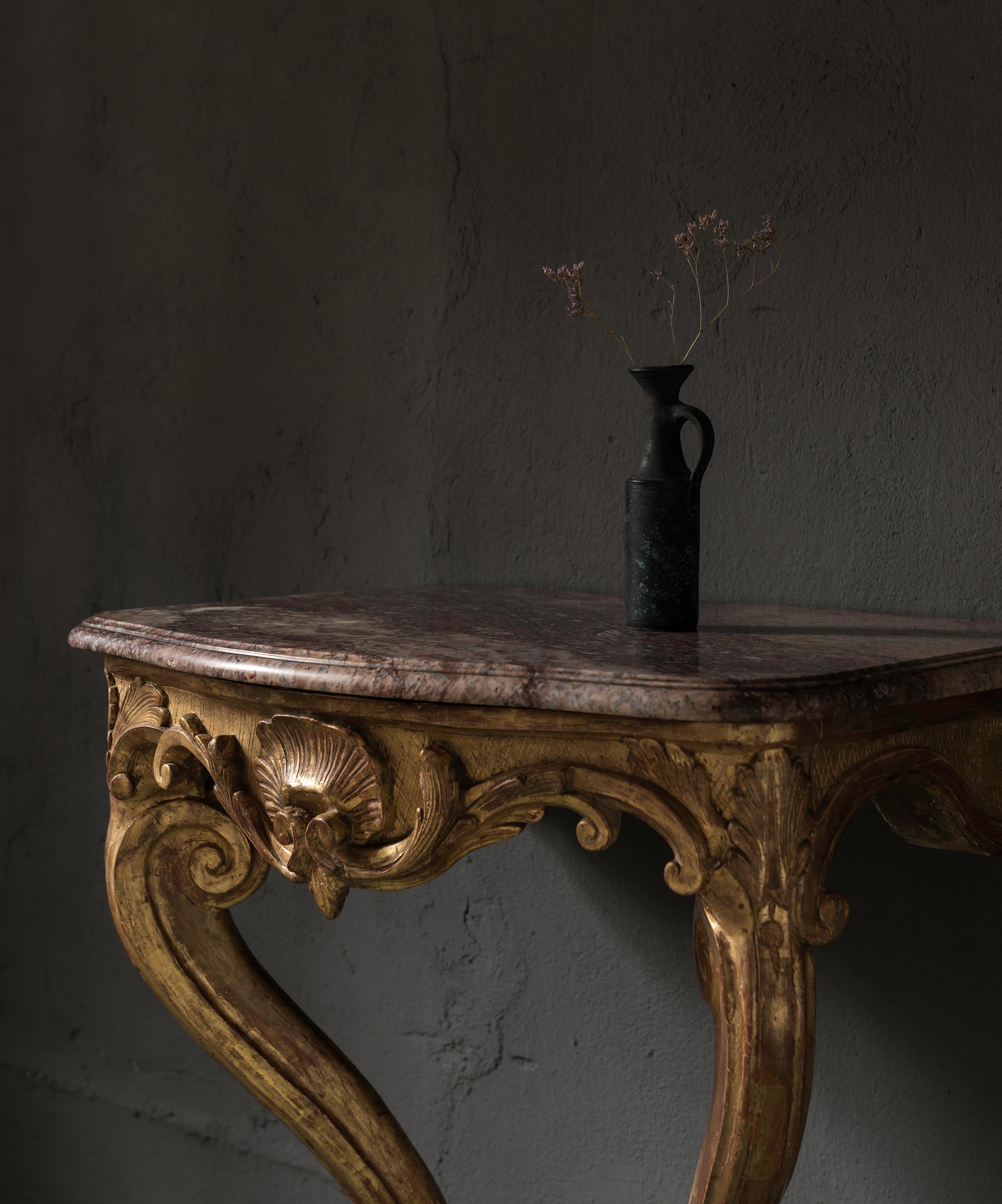 A very elegant small console in beautifully patinated carved giltwood. 
Beautifully shaped corners of the reddish marble top.
Soft lines as typical for the Louis XV period.  
Due to its sculptural presence, the console works in modern and minimal as