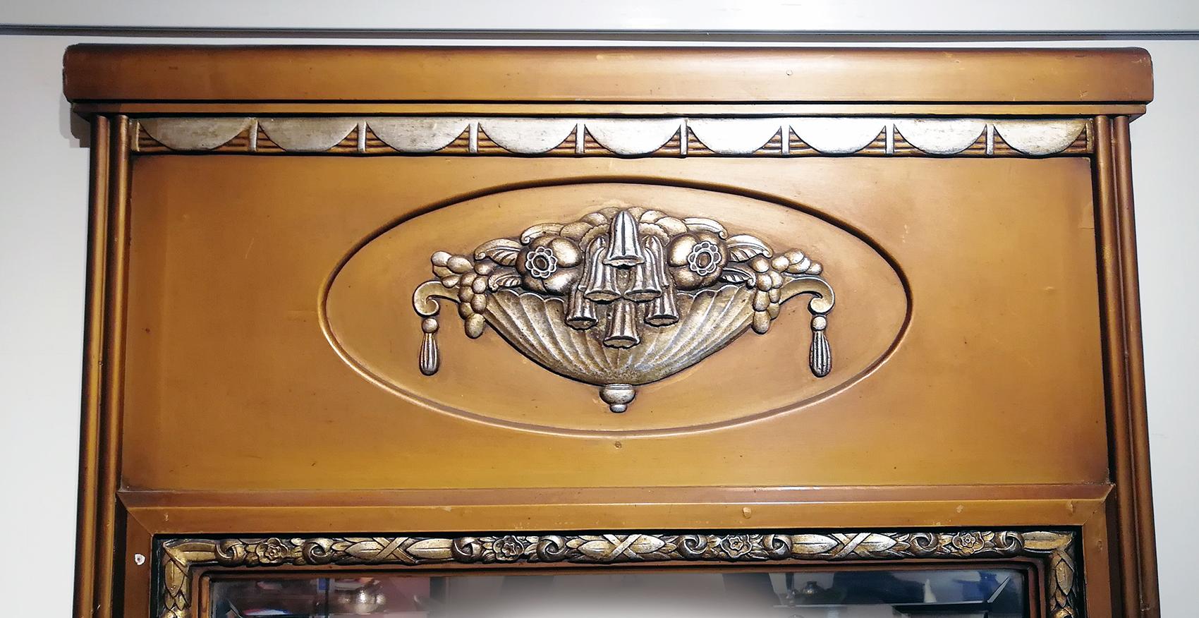 Large French Art Deco wall mirror made of wood and mirror with gilt frame and etched decorative silver flower basket in the upper section. The mirror is surrounded by silver floral motif design on three of its sides.