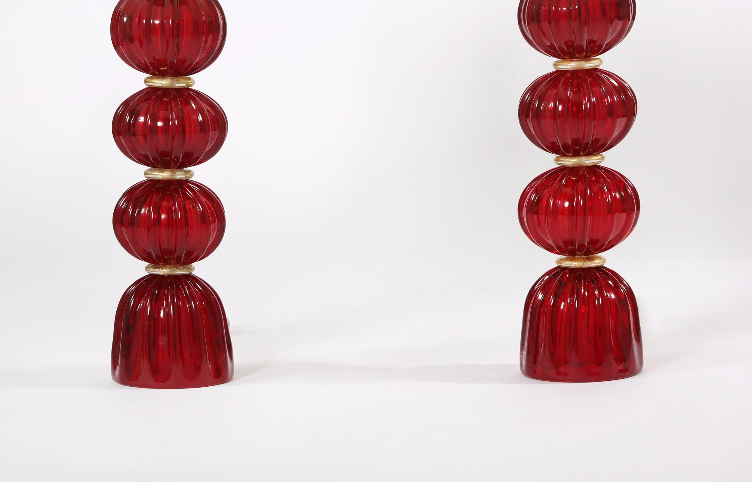 Very exquisite pair of red with gold details Murano glass table lamps. Each lamp is in great working condition. Rewired for use in the U.S. No special light required. Maker's mark undersigned. Each lamp come with a round drum silk exterior shade 11