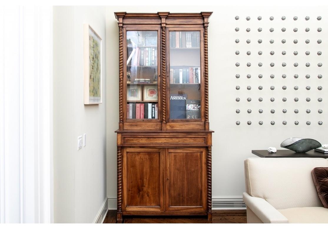 A tall bibliotheque made in two parts with Barley Twist supports. The top with carved angular cornice details and double glazed doors with four adjustable interior shelves. The interior sides in old pale Mint paint. The lower projecting cabinet with