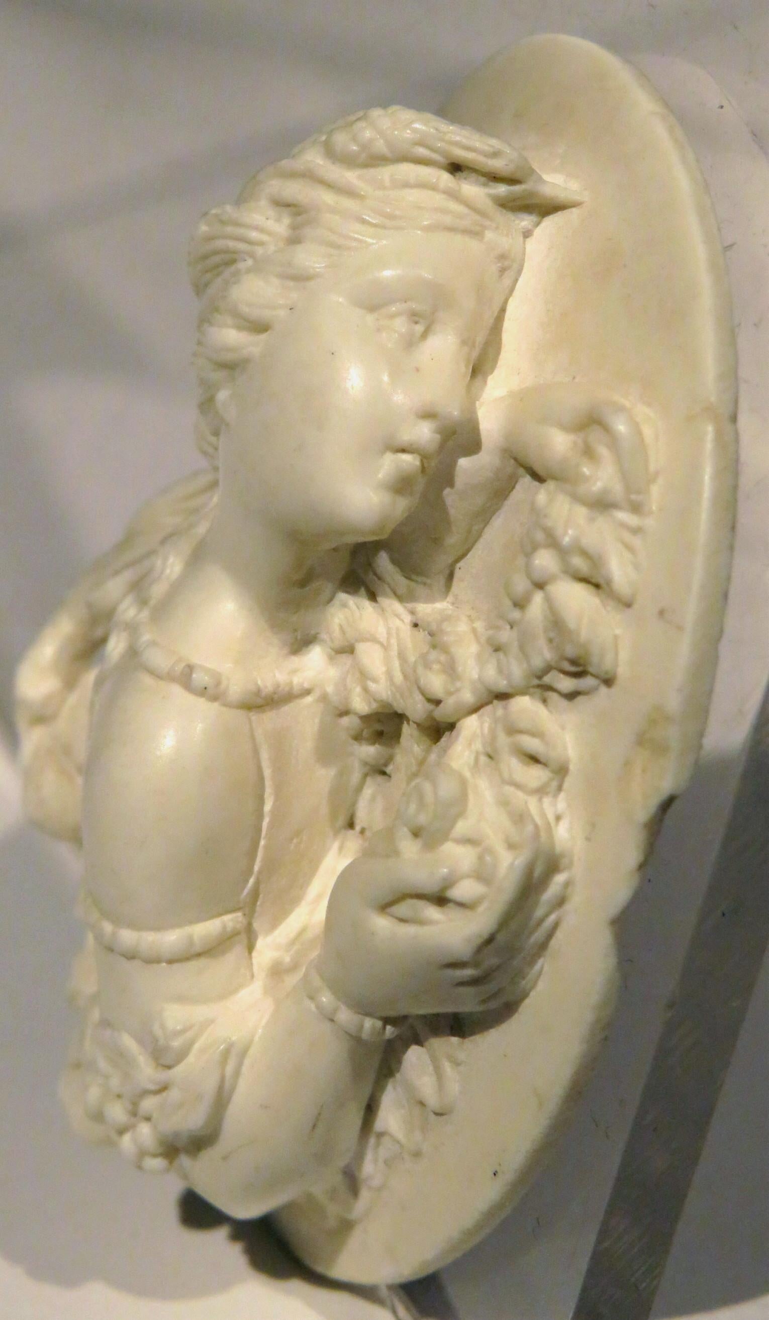 A finely executed lava cameo, sculpted in high relief with exacting proportions and detail, depicting a beautiful young woman rendered in profile against a field of trailing, fruiting vines.
