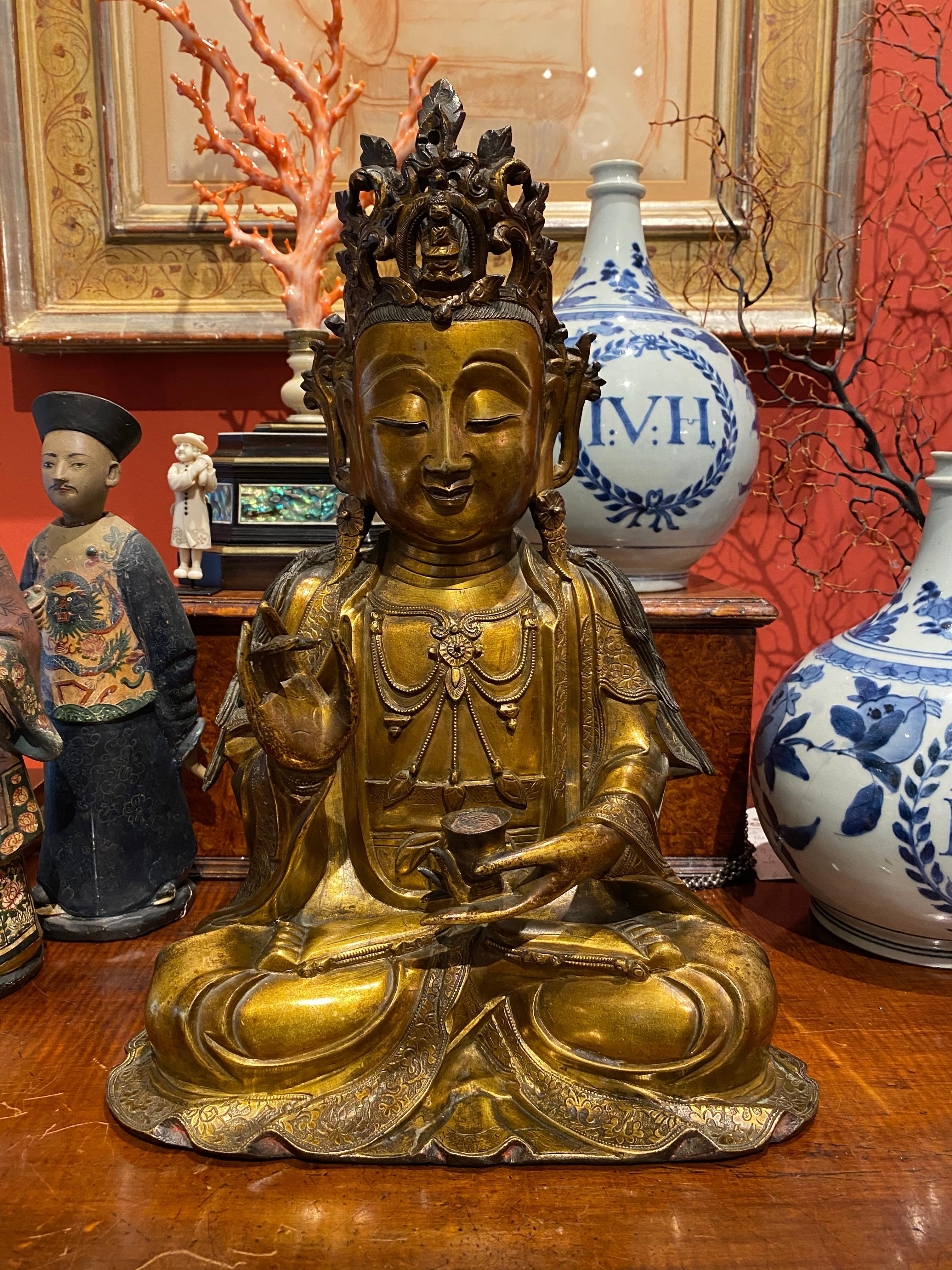 A very fine Chinese gilt bronze figure of Guanyin

Ming dynasty, late 16th-early 17th century

The deity seated in padmasana, the right hand raised in Karana mudra and the left holding a cup, dressed in long robes decorated with flowers at the