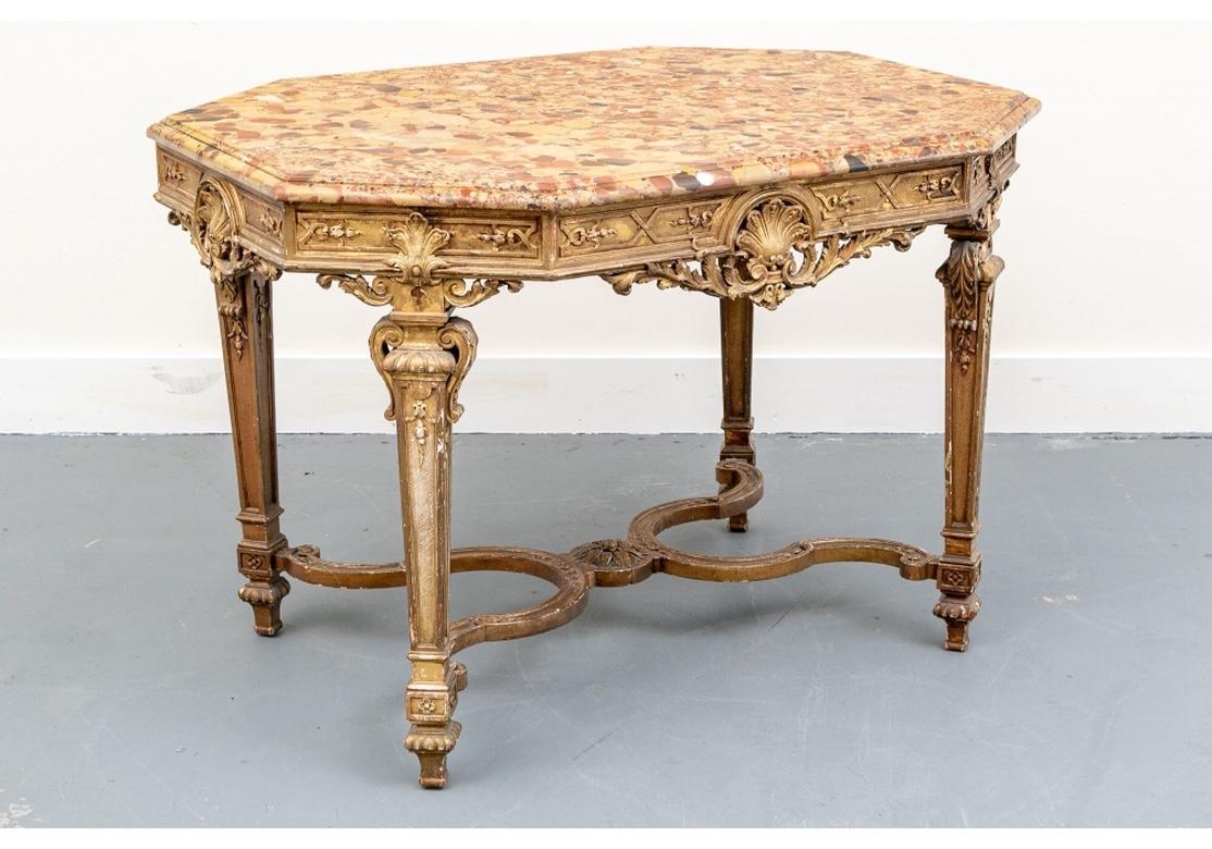 The shaped table with canted corners and elaborately carved frame. The apron sides with large carved and gilt palmettes and scrolled acanthus leaves in openwork frames. The corners with different style palmettes in relief, all with framing raised