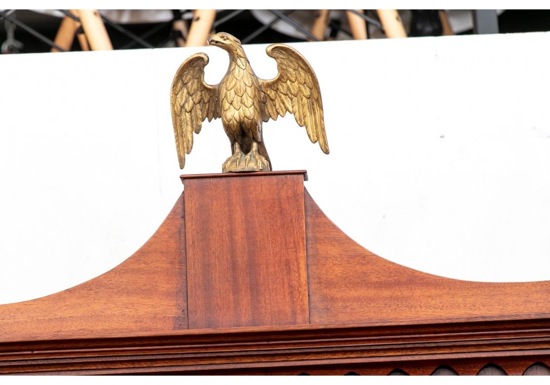 Well constructed with fine mahogany veneer with Federal style brass eagle finial on a pedestal. The carved cornice with urn form finials over a carved frieze. Two glazed doors with mullions flank the projecting center one, with two wood shelves and