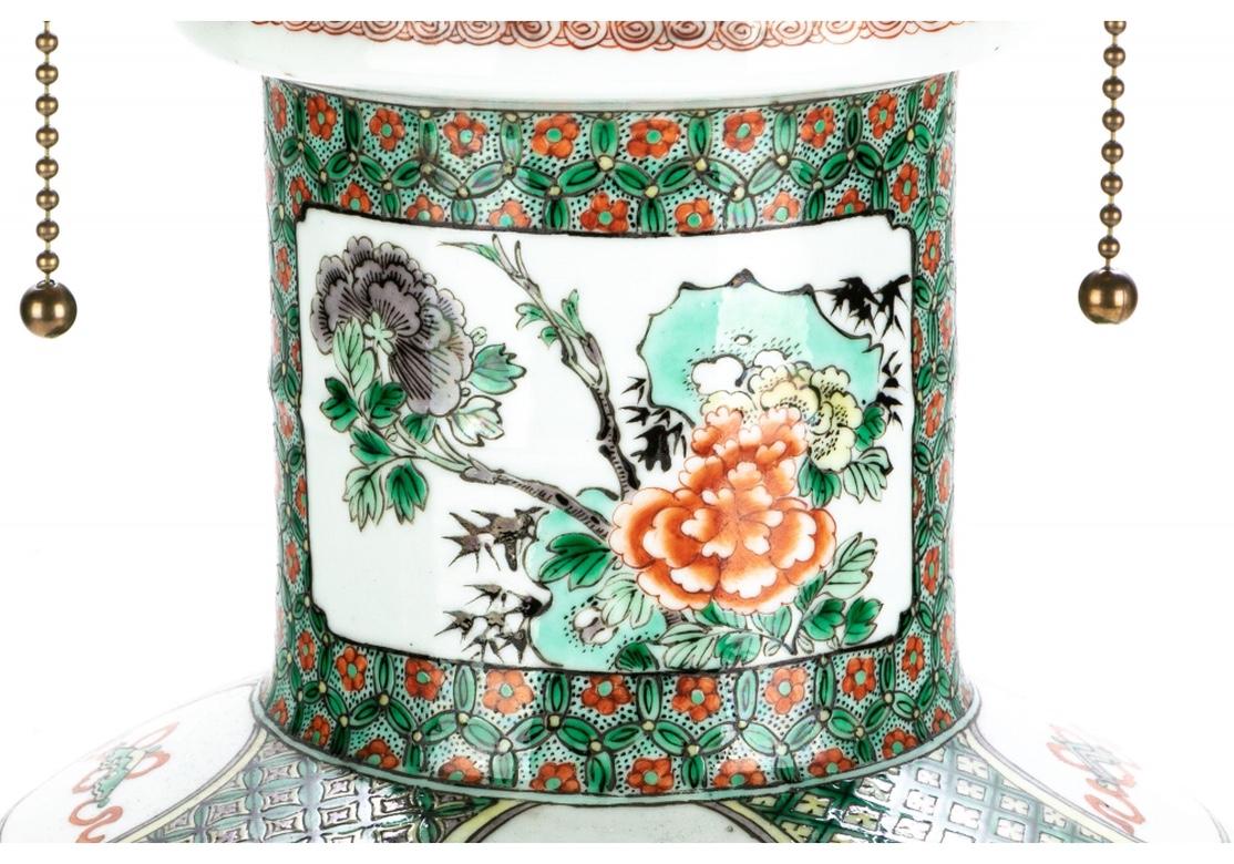 Chinese porcelain vase mounted as a lamp with a round tiered gilt bronze or brass base embossed with berries and leaves. The lamp with cameos and panels of florals and birds that are on a field of red flowers within green wreaths with a slight