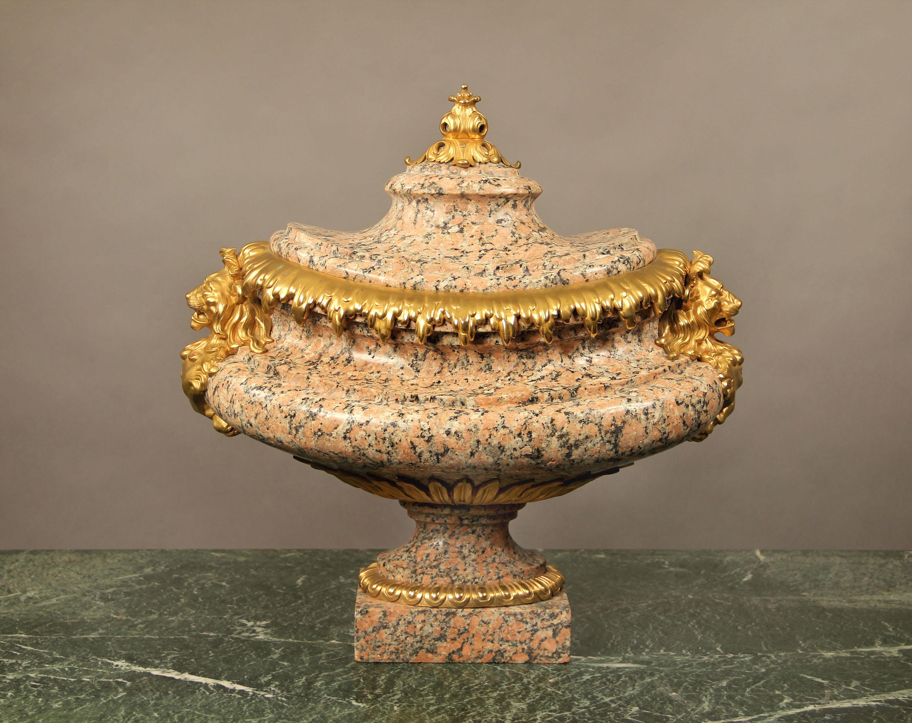 Un raffinato centrotavola francese della fine del XIX secolo in granito rosa e bronzo dorato,

di forma ovale, i lati con maschere di leone e la parte superiore incurvata sormontata da una bacca e da un acanto.