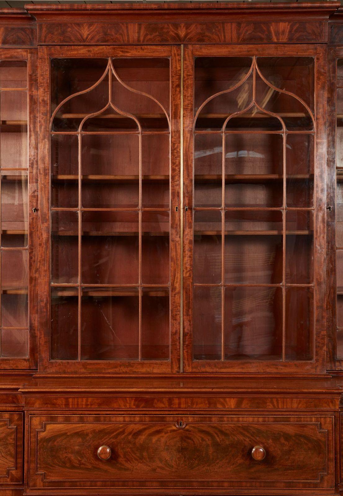 Very fine George IV mahogany breakfront bookcase having molded cornice with flame grain panels over glazed doors, the two center doors with Gothic astragal glazing over three drawers, the center with butler's secretary drawer over cupboard doors,