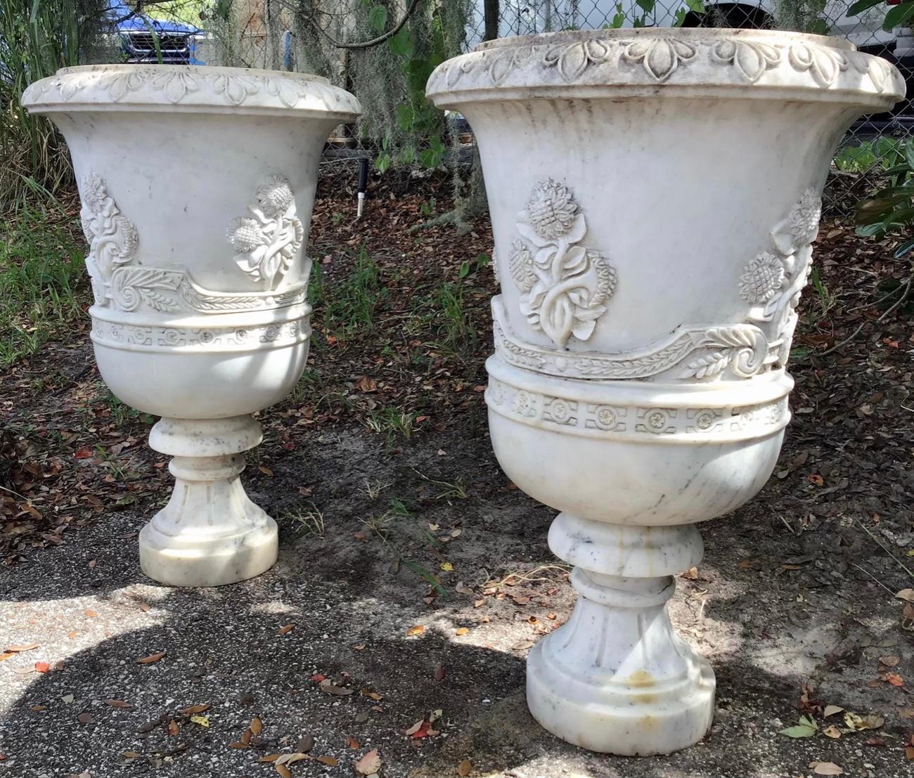 A very fine pair of hand-carved Carrera marble urns. Over sized and intricately designed with a carved rim and the body with large sunflowers and other intricate details. Approximately 250 Lbs each.