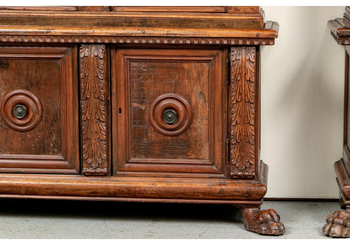 Two-part cabinets, the tops with egg-and-dart and fluted friezes over fluted pier supports with leafy capitals. With grille work doors and side panels, three carved inside shelves. Mounted on cabinets with carved acanthus leaf supports, double doors