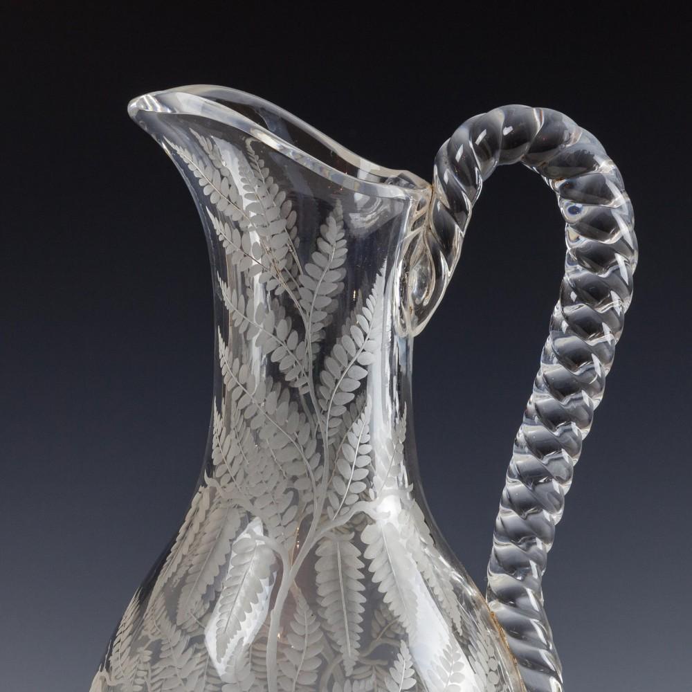 Heading : Engraved glass Ewer
Period : Victorian
Date : c1880
Origin : England
Colour : Clear
Bowl : A barley twist handle. Finely engraved with ferns below an acacia type tree, a further sapling beneath the handle
Foot : Star Cut
Glass Type :