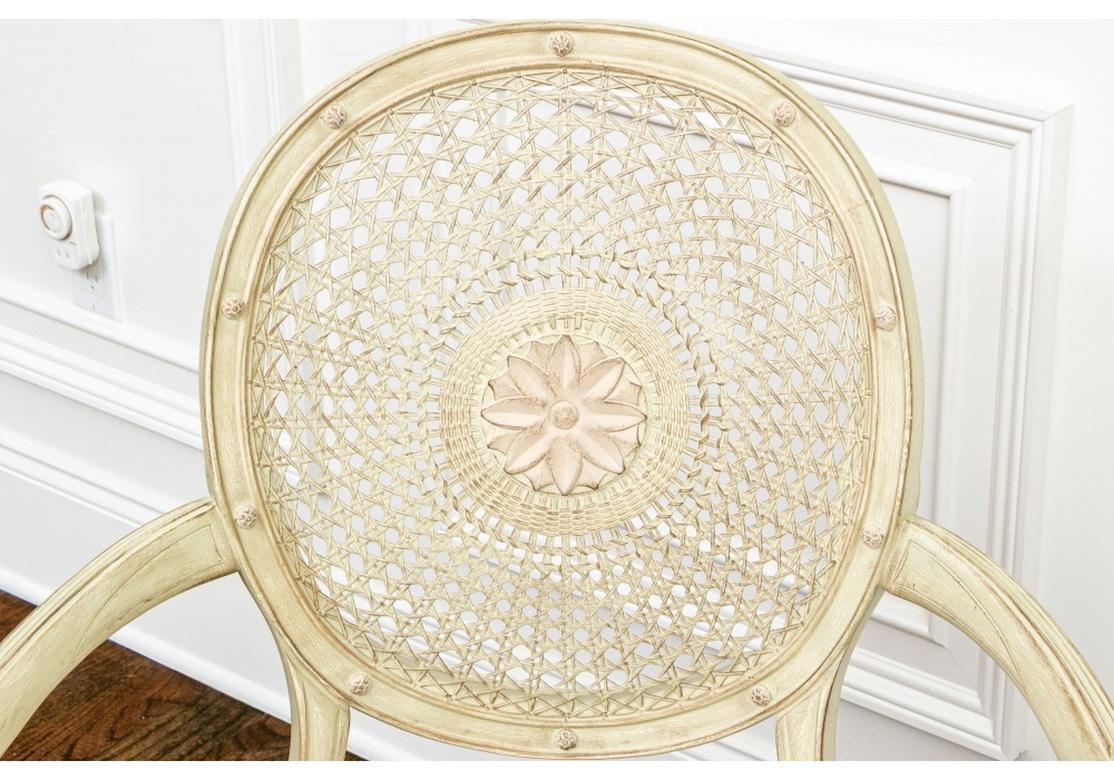 A particularly fine pair of Spider-Back chairs with meticulous and sensitively tailored upholstery and trim. Elegant fauteuils in pale greenish-cream paint. The caned round backs with carved center rosettes and bosses on the frames. The curved arms
