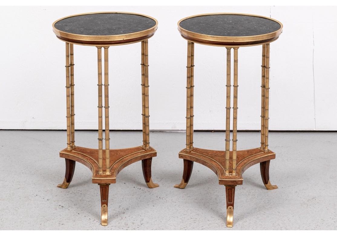 Fine neoclassical style circular bronze stands with black marble tops. Raised on three double faux bamboo form bronze legs mounted on an incurved tripod base in figured wood. With thin detailed ribbed gilt bronze trimmed bands and edges. Raised on