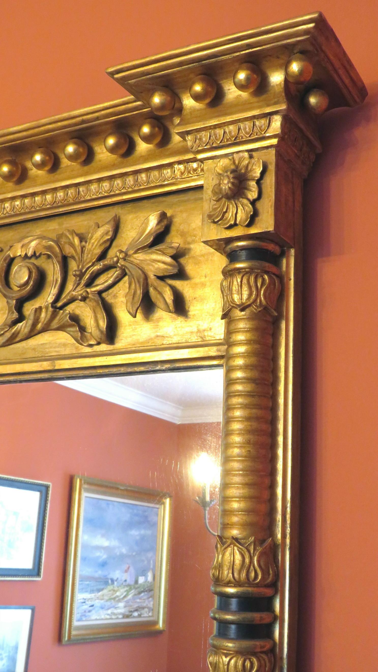 An outstanding Regency period giltwood over-mantel mirror featuring an architectural cornice decorated with hand-applied gilt spherules, overtop a panel with applied foliate elements in high relief above a later rectangular plate flanked by ringed