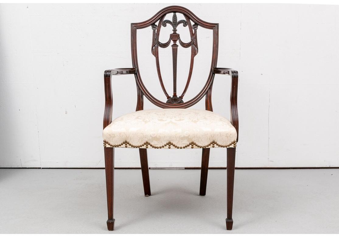 An elegant set with particularly attractive graining. With two arm and six side chairs. The carved ribbed mahogany frames in a dark stain. The shield backs with Prince of Wales feather motif on the tops of the openwork splats with urn and swag