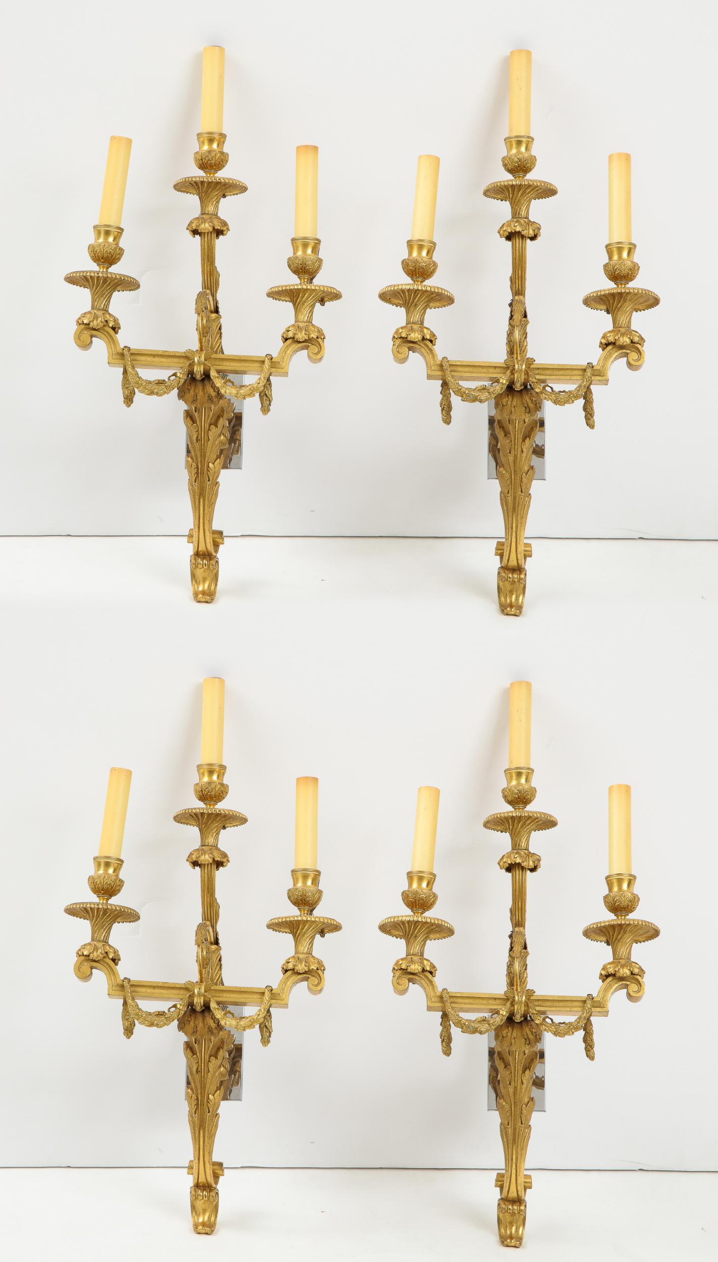 Fine and rare set of four 18th Century Louis XVI fire gilt bronze three light wall lights, the bobeches with acanthus leave details over spiral fluted and flared drip pans, joined by strapwork arms having draped garlands and scrolled acanthus leaf