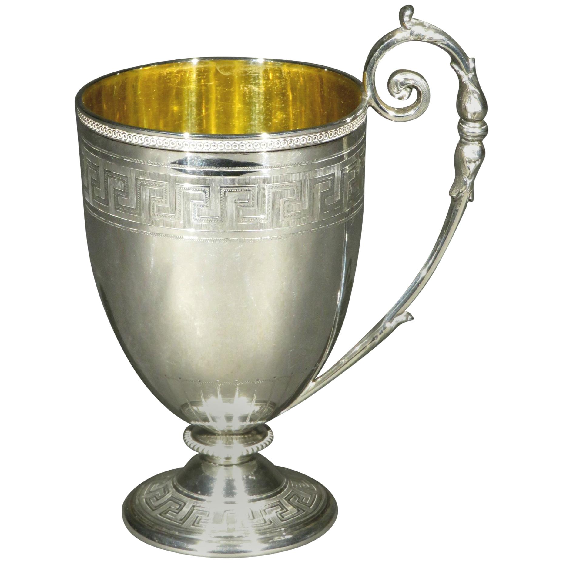 Une exceptionnelle tasse de baptême en argent sterling de style néoclassique, présentant un élégant bol en forme de gobelet décoré d'un bord perlé guilloché, au-dessus d'une bande de motifs gravés de clés grecques. 
L'intérieur présente une surface