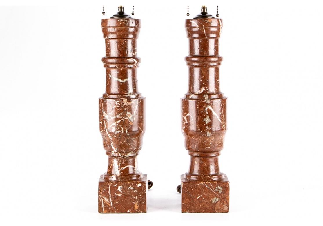 A notable pair of tall vintage turned red marble lamps in all original very good condition. The form is a tall urn type shape and the marble is a deep clay red with many white striations. Quality hardware is in a deep antique brass finish. Probable