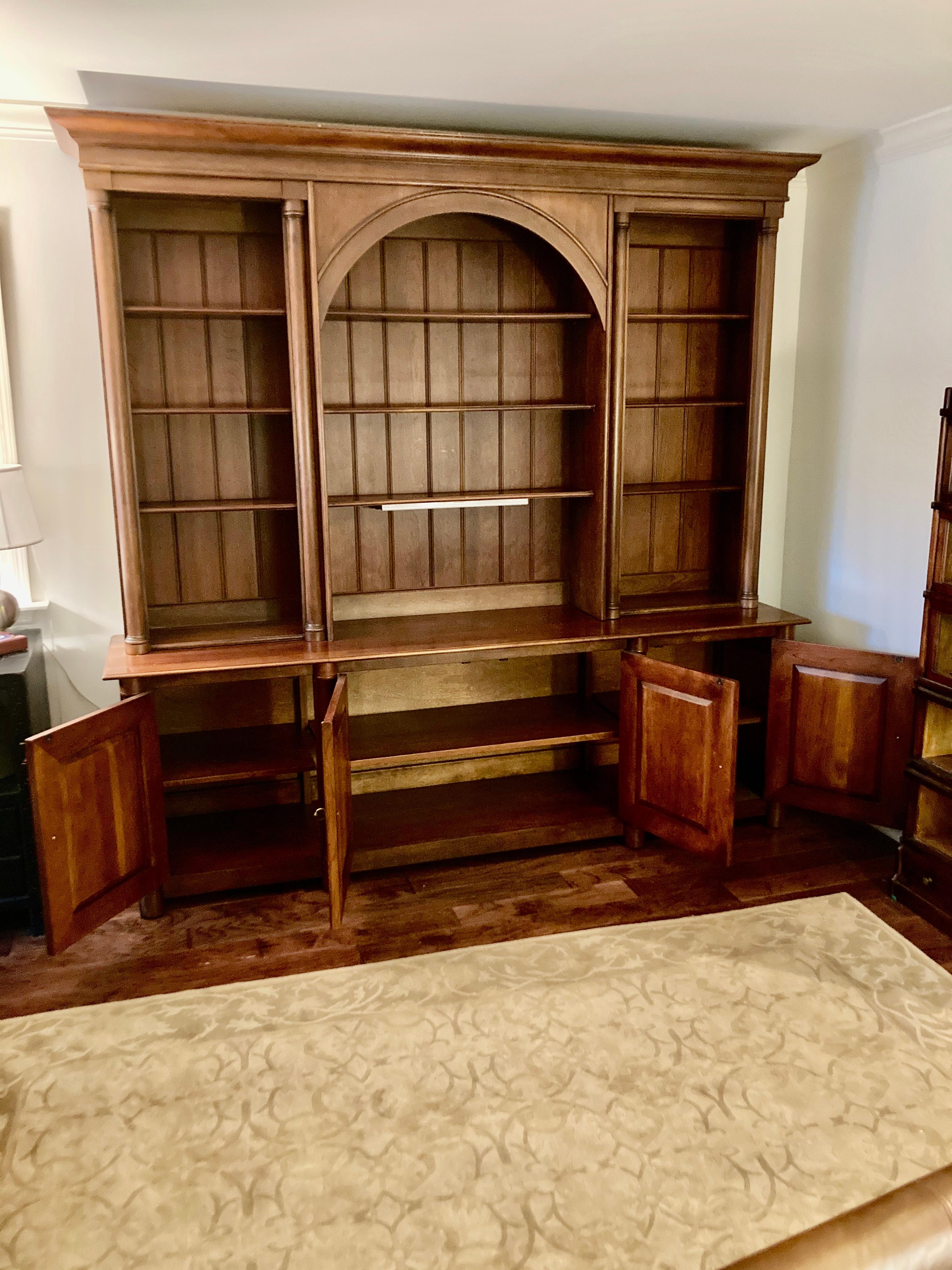 Grand cherry triple bookcase credenza breakfront having bottom credenza with 4 panel doors and tons of storage, top bookcase with adjustable shelves and handsome central arch and crown molding. A recessed light illuminates center section of bookcase