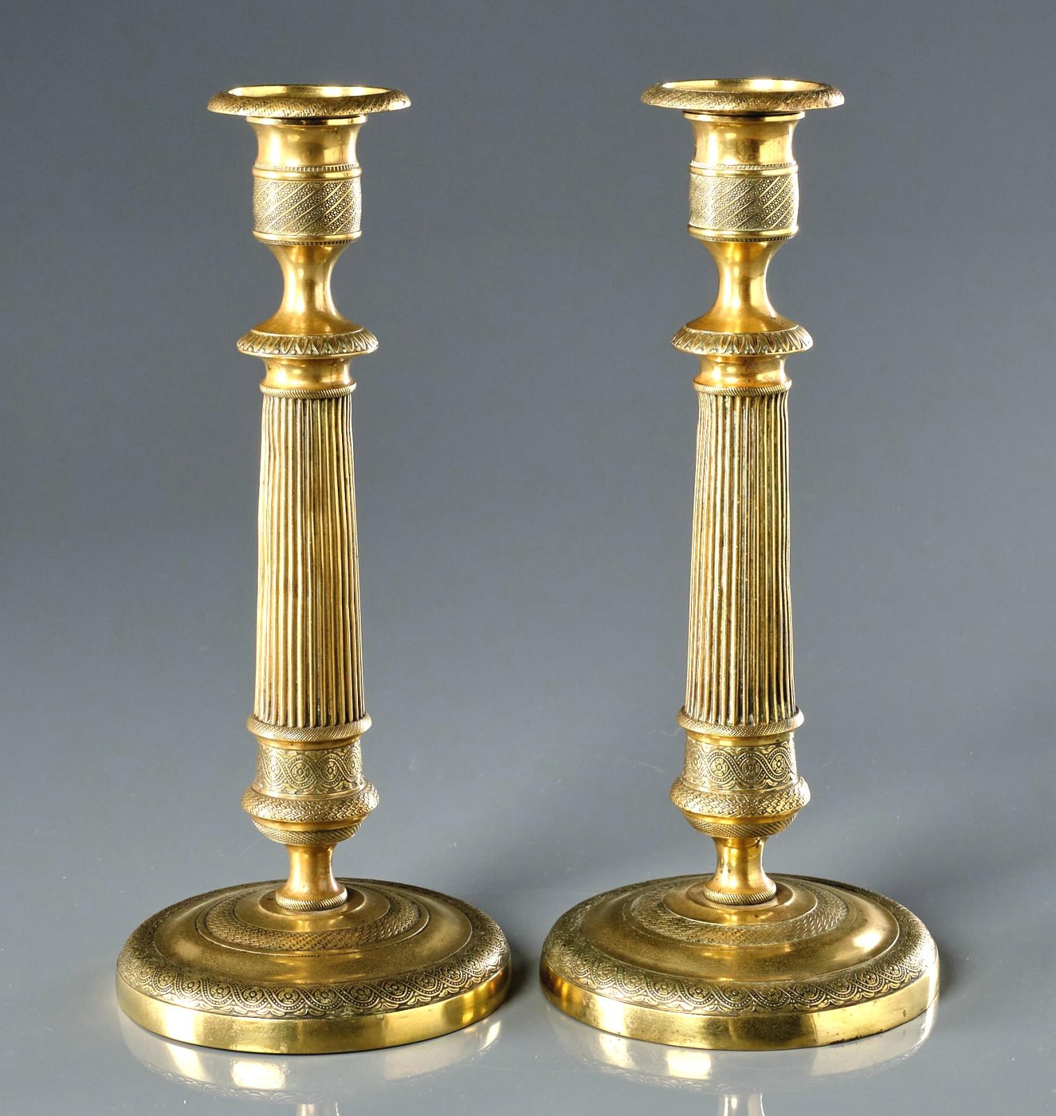 Ein sehr hübsches und hohes Paar vergoldeter Messing-Kerzenständer aus dem frühen 19. 
Beide zeigen geriffelte Säulen, die sich von runden, mit fein ziselierten Motiven verzierten Sockeln erheben, und ähnlich adressierte, urnenförmige Tüllen mit