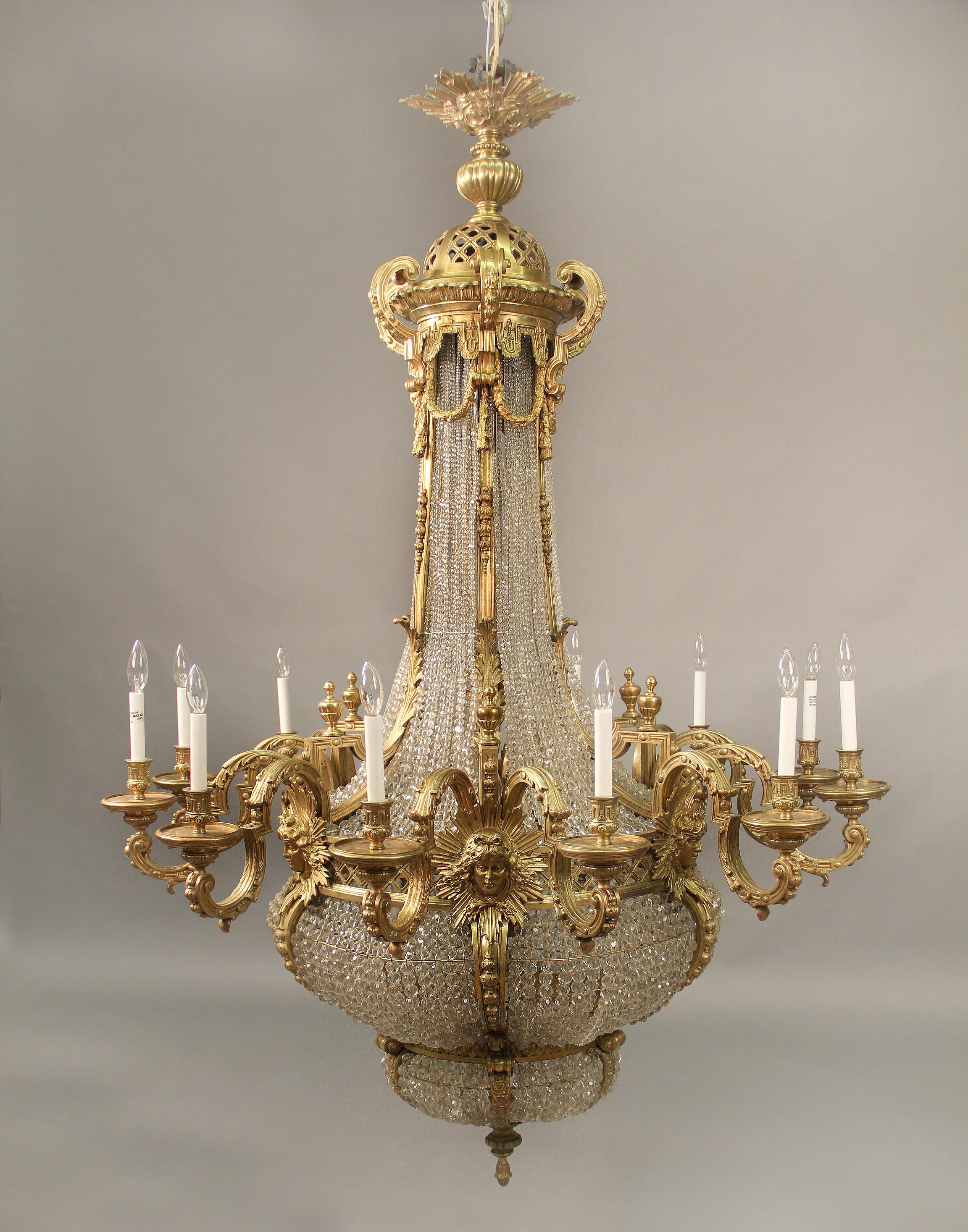 A very impressive and palatial late 19th century gilt bronze and crystal twenty four light basket chandelier

The large sunburst corona above a reticulated pierced crown adorned with bronze curtains and garlands, long beaded neck leading to a