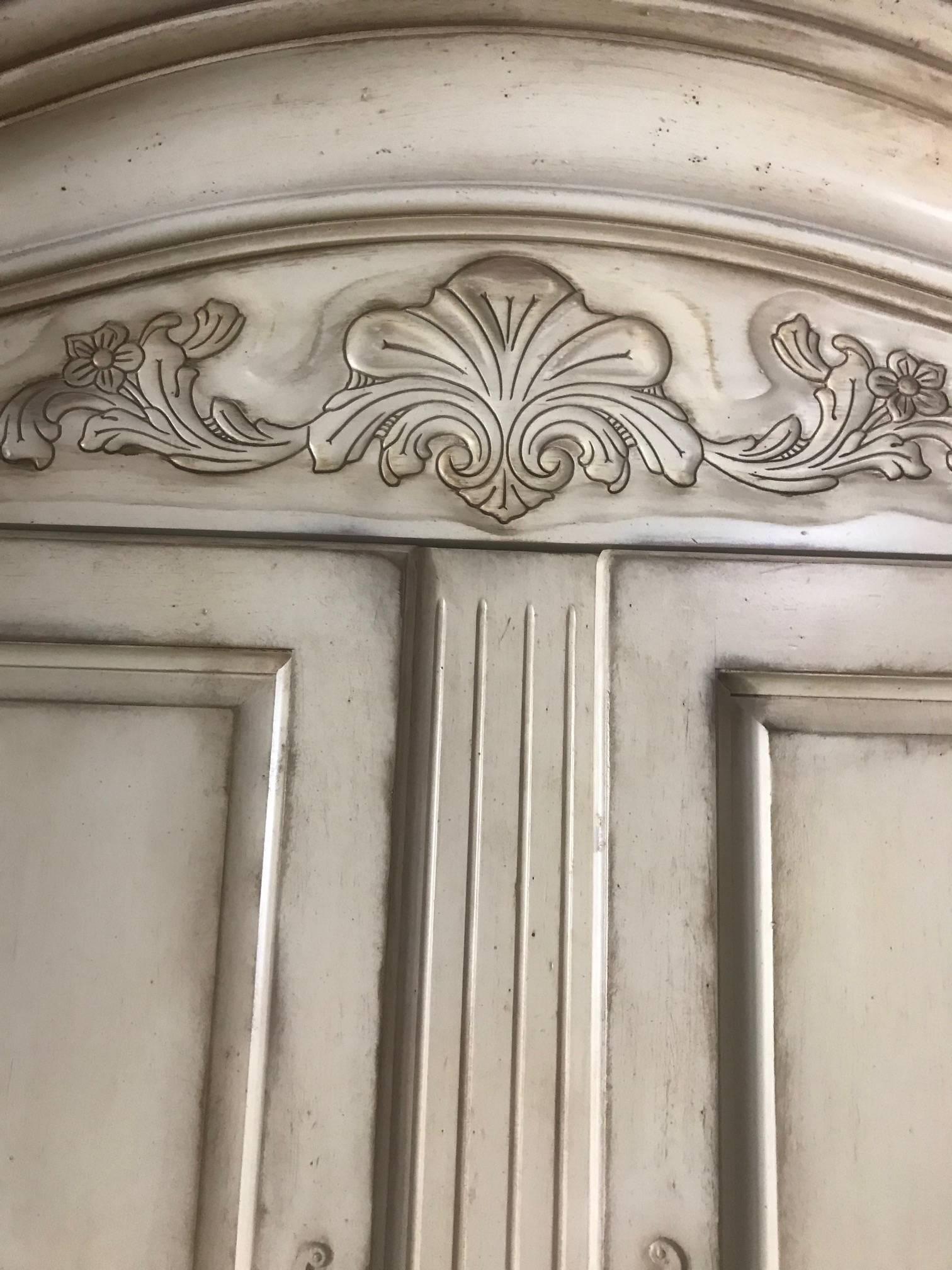 Very large free standing century Cantal armoire having a special cream antiqued Biscay finish with carved wood decoration and four-panel doors. The large doors open to reveal a space that was outfitted for a television, but could be reconfigured