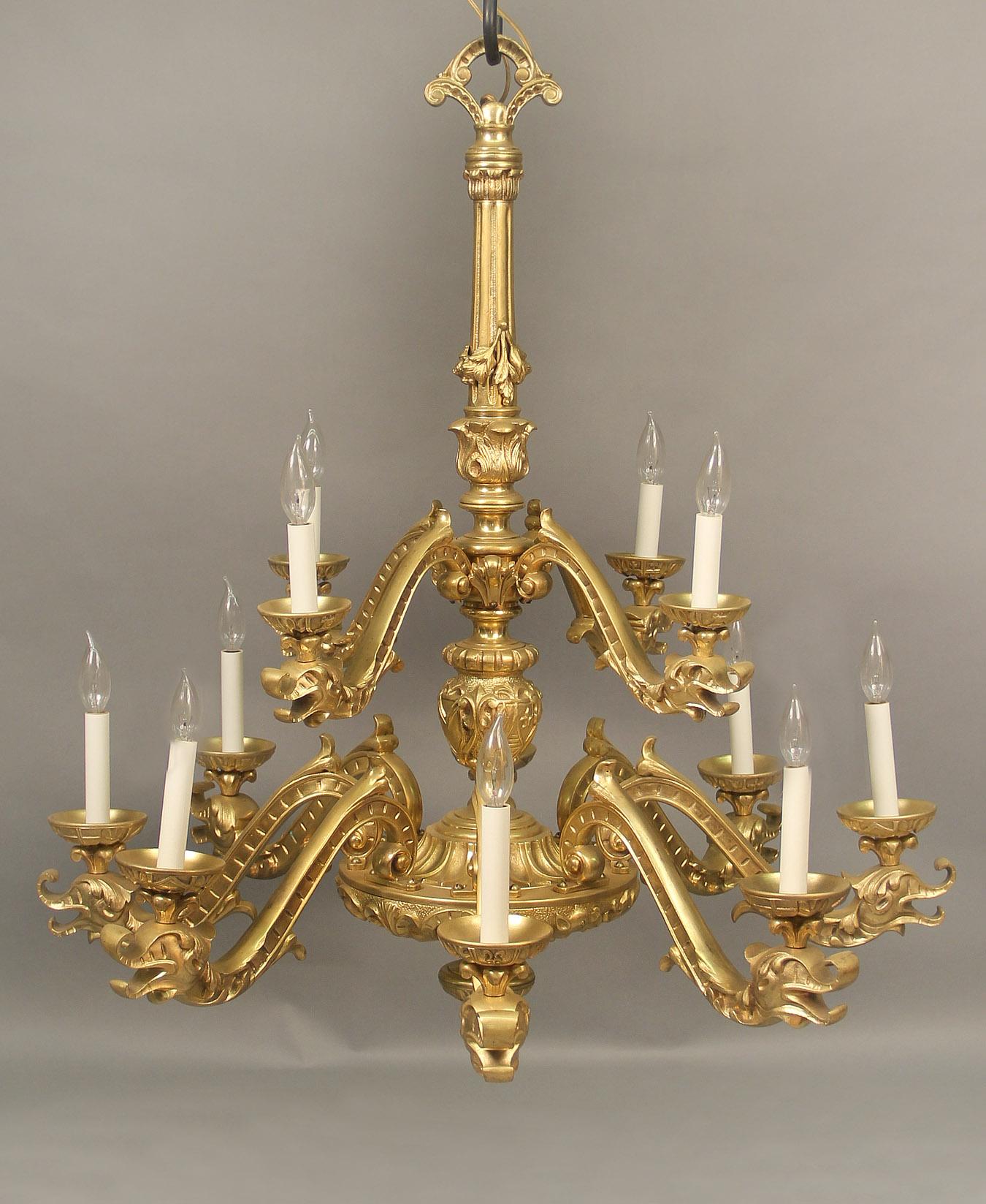 An Very Interesting Late 19th Century Gilt Bronze Twelve Light Chandelier

The long neck winding down to a flame and a small tier of four arms, the body intricately designed with fleur de lis and leading to a larger tier with eight arms, each of the