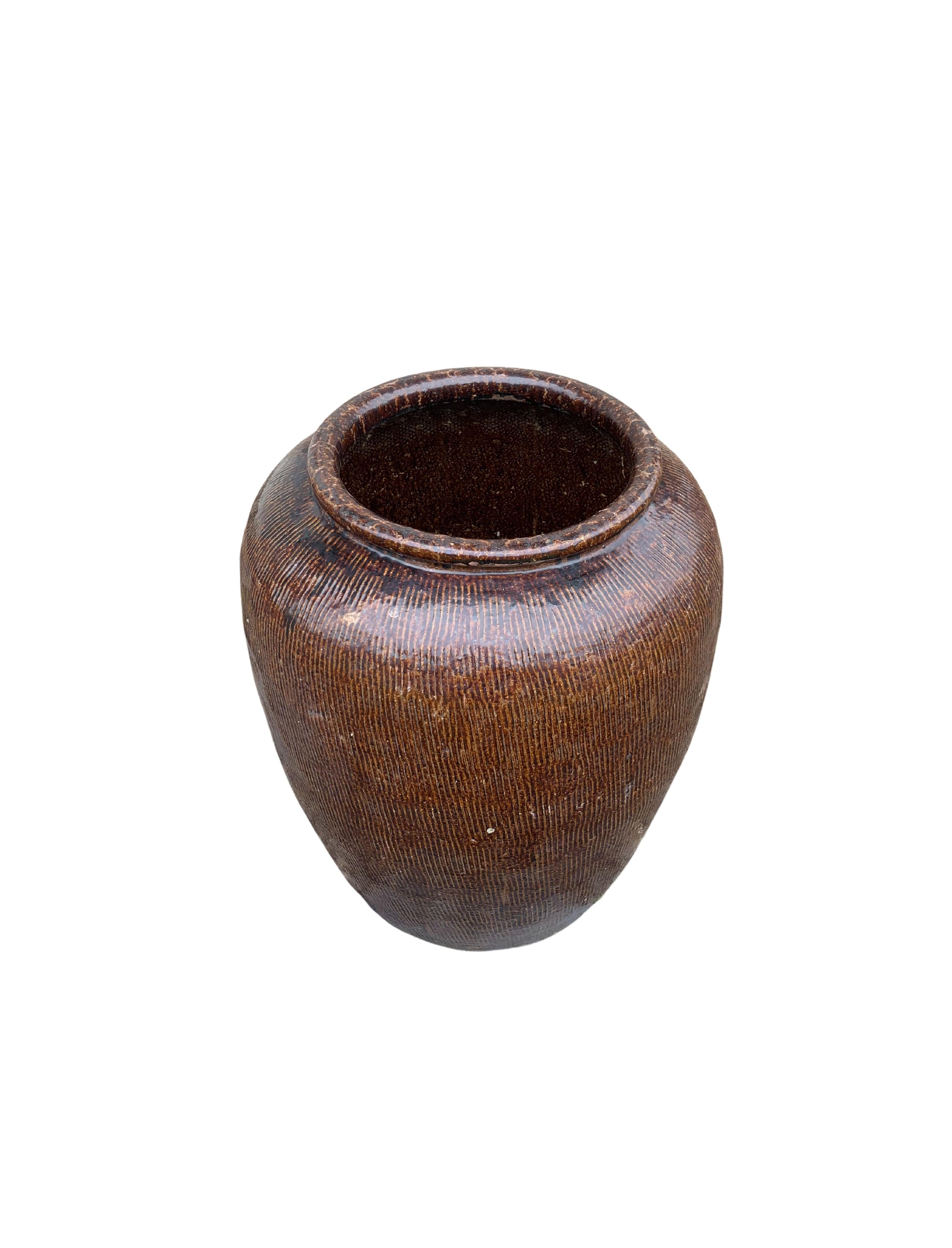 This glazed Chinese ceramic jar from the turn of the 19th century was once used for soy sauce production. It features a brown finish and outer surface that features a ribbed texture. A great example of Chinese pottery, with its imperfections and