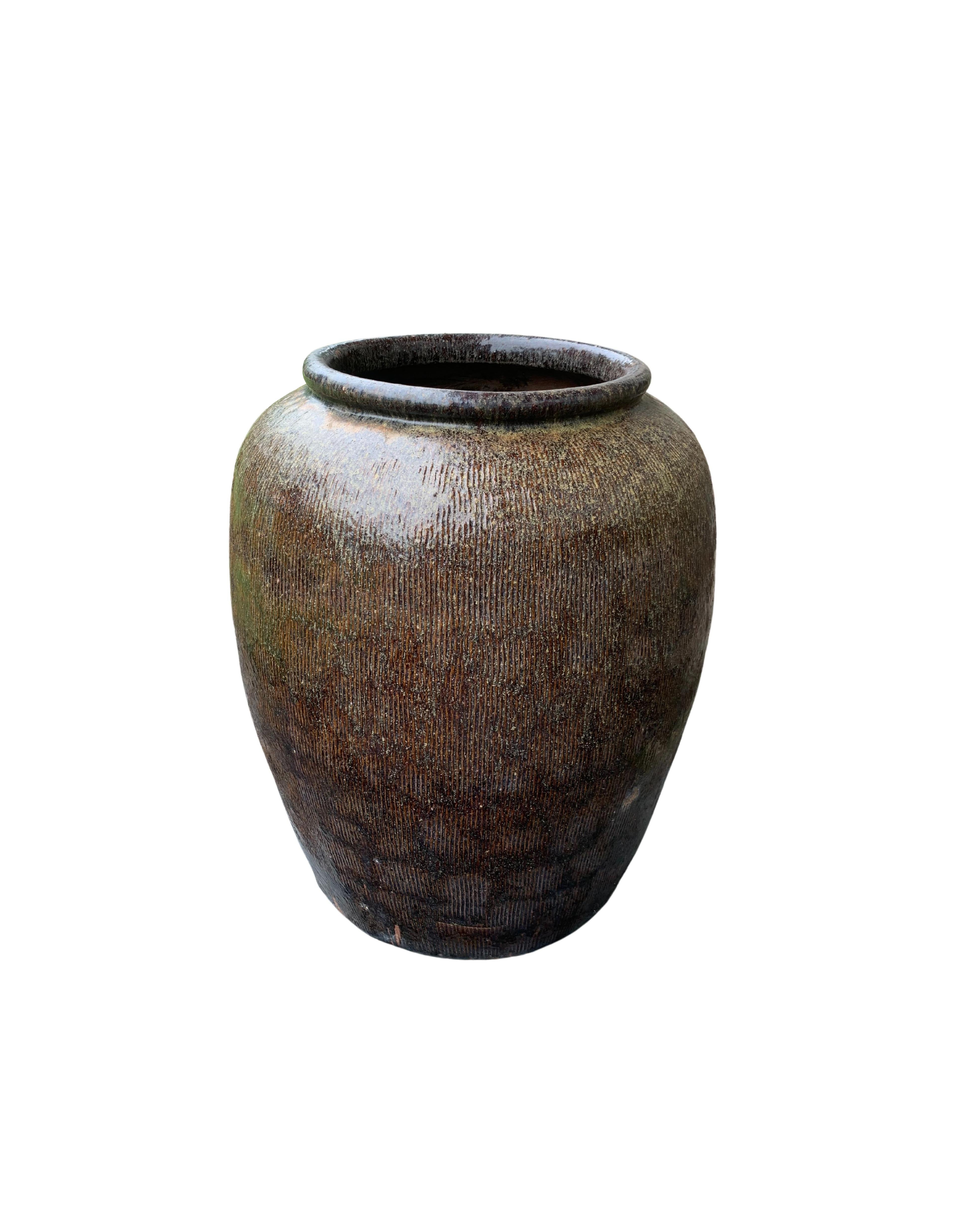 This glazed Chinese ceramic jar from the turn of the 19th Century was once used for soy sauce production. It features a brown finish and outer surface that features a ribbed texture. A great example of Chinese pottery, with its imperfections and