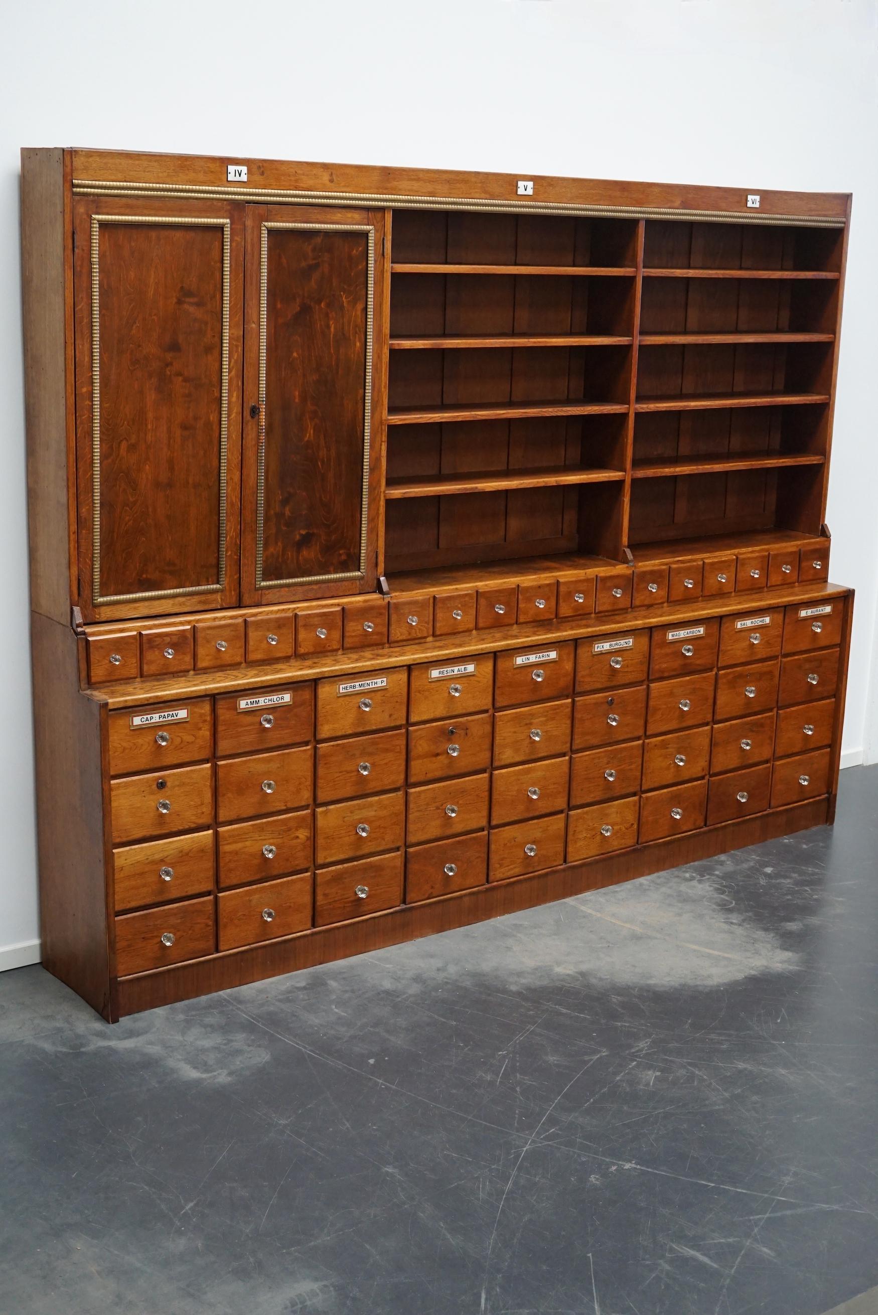 This apothecary cabinet was produced during the late 19th century in the United Kingdom. It features 36 large drawers and 18 small ones with glass knobs. The top cabinet has two doors and many shelves. The interior dimensions of the large drawers