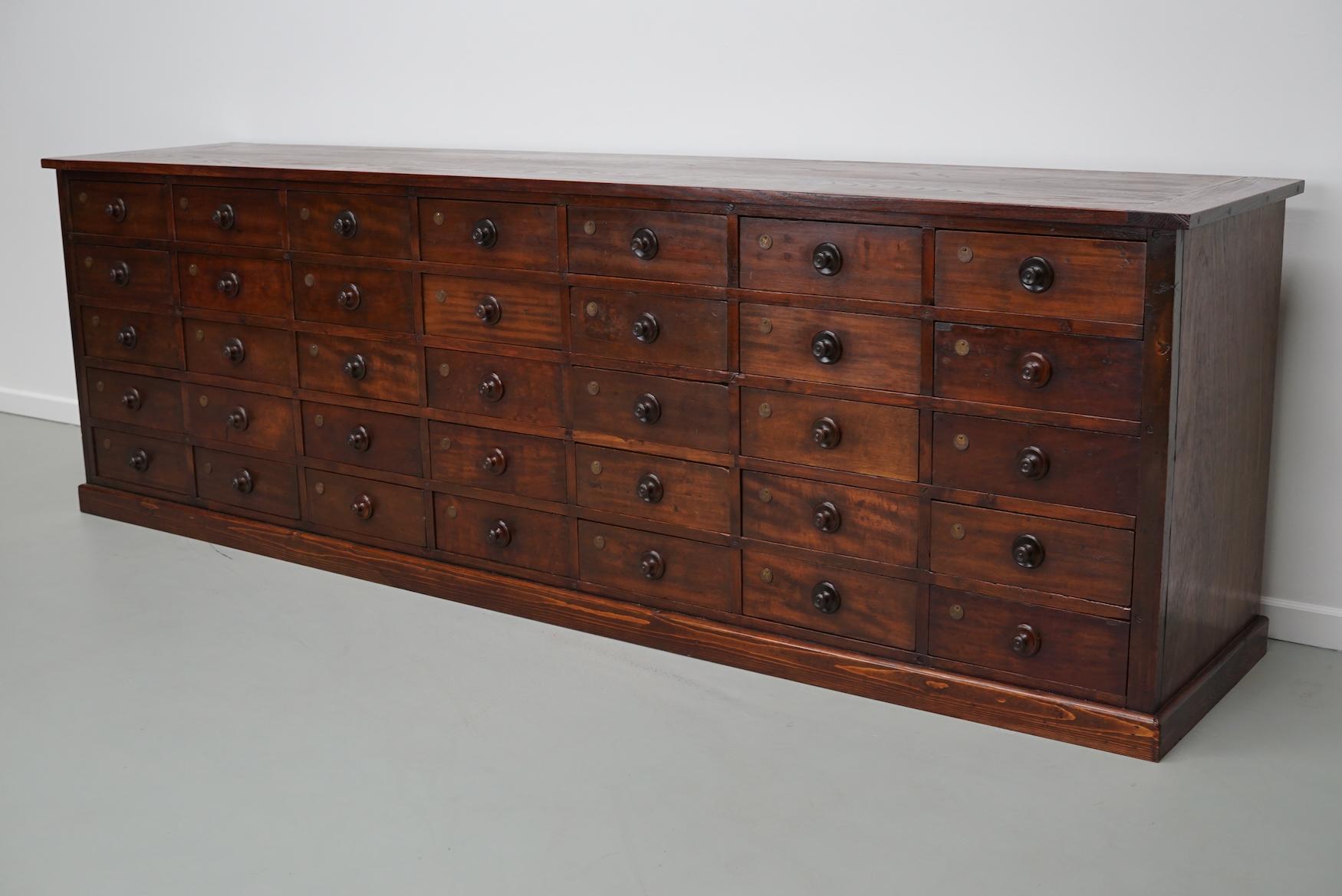 This apothecary bank of drawers was designed and made in Belgium and used in a hardware store in Antwerp. It is made from solid wood with wooden knobs and brass numbers. The cabinet has retained a rich patina with some natural distressing. The