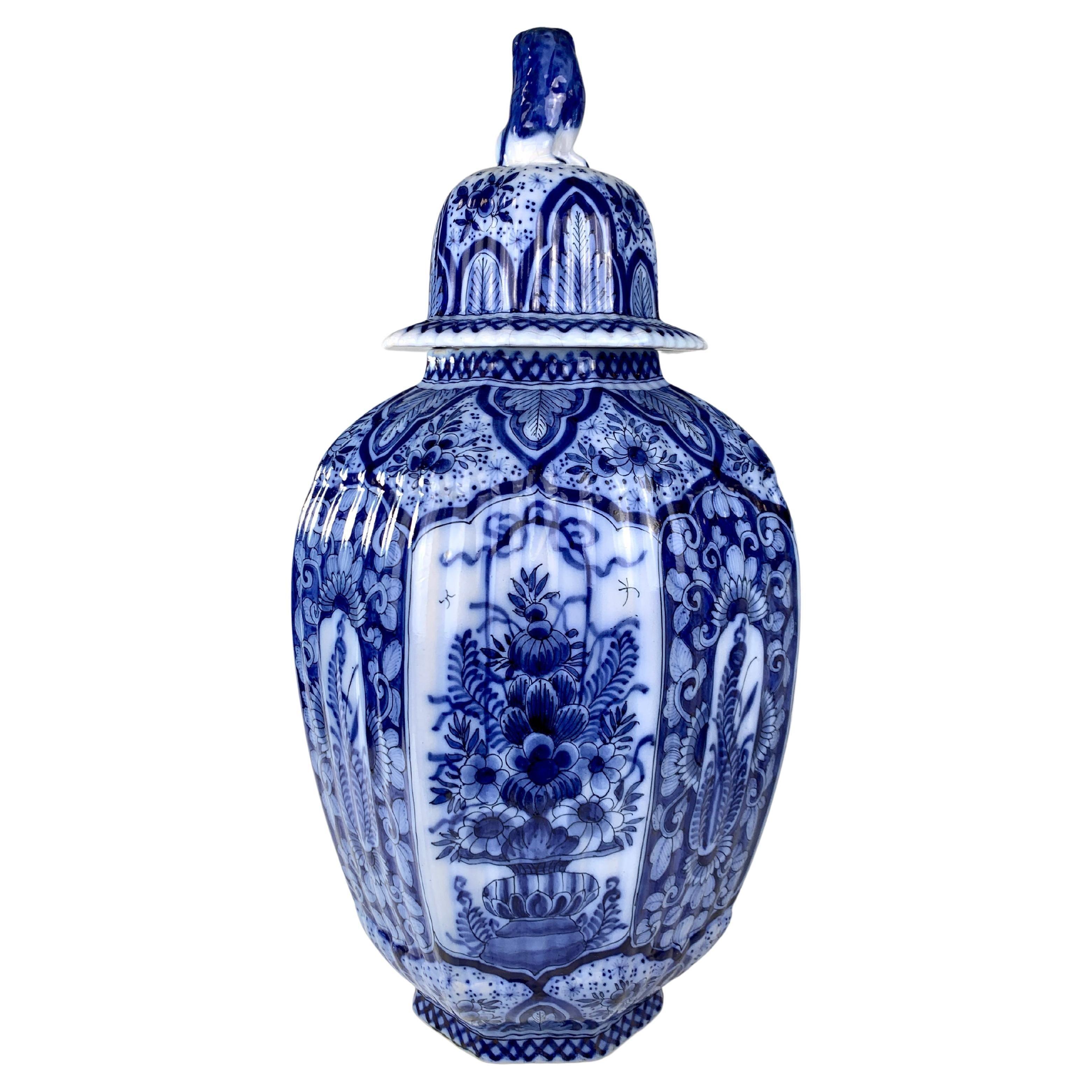 This fabulous Delft jar is painted with traditional deep cobalt blue on a tin-glazed ground.
The jar has six panels, which alternate between flowers in a basket and ferns with scrolling vines.
Large blue lappets decorate the shoulders and cover.
The